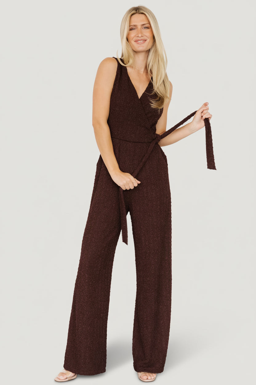 Front view of model wearing Natasha Jumpsuit in espresso, showing surplice neckline, adjustable side tie and wide-leg silhouette in crepe fabric.