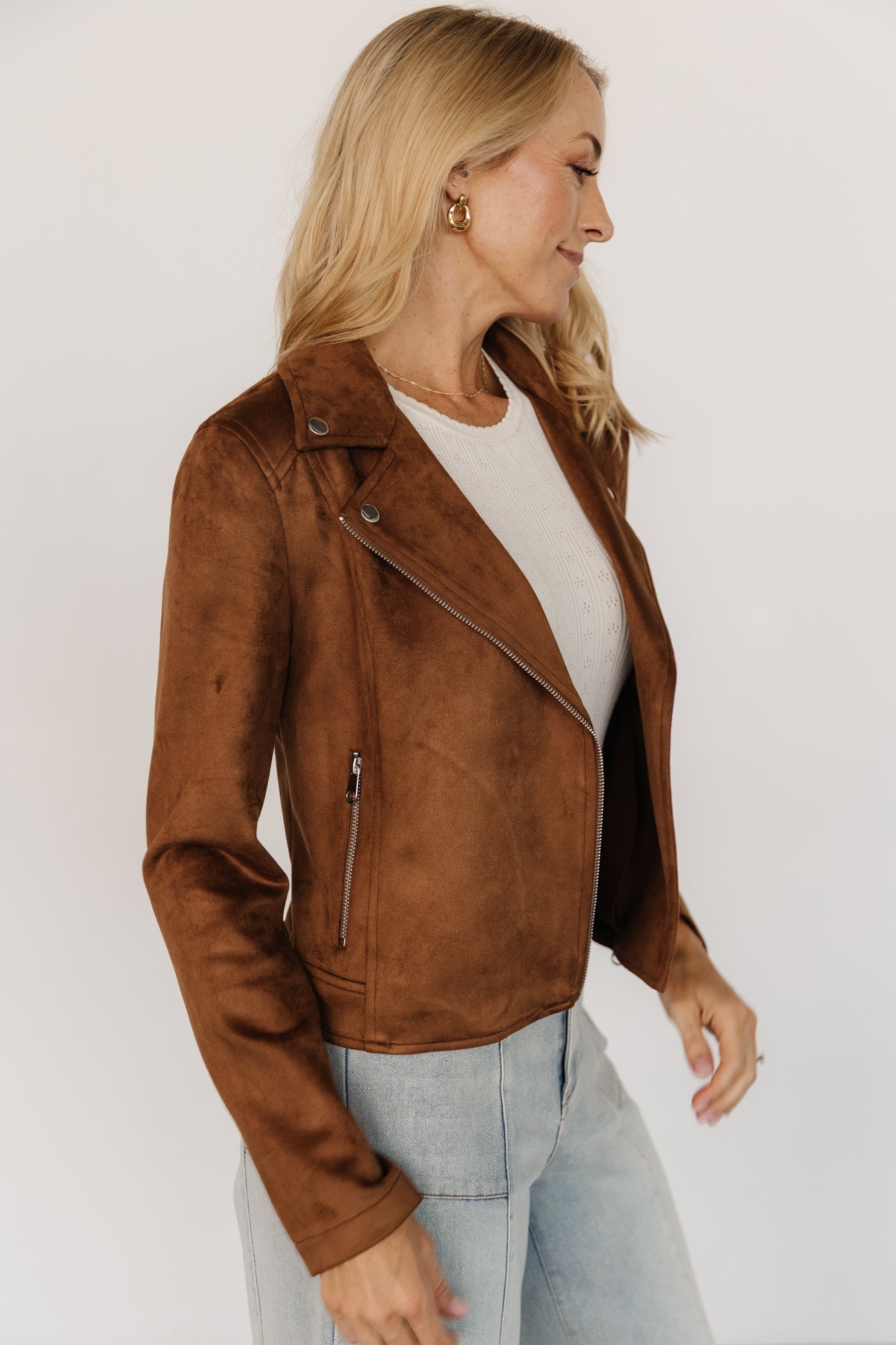 Back and hem detail of the Marisa faux suede moto jacket in caramel, showing the snap belt straps and clean cropped finish on the model.