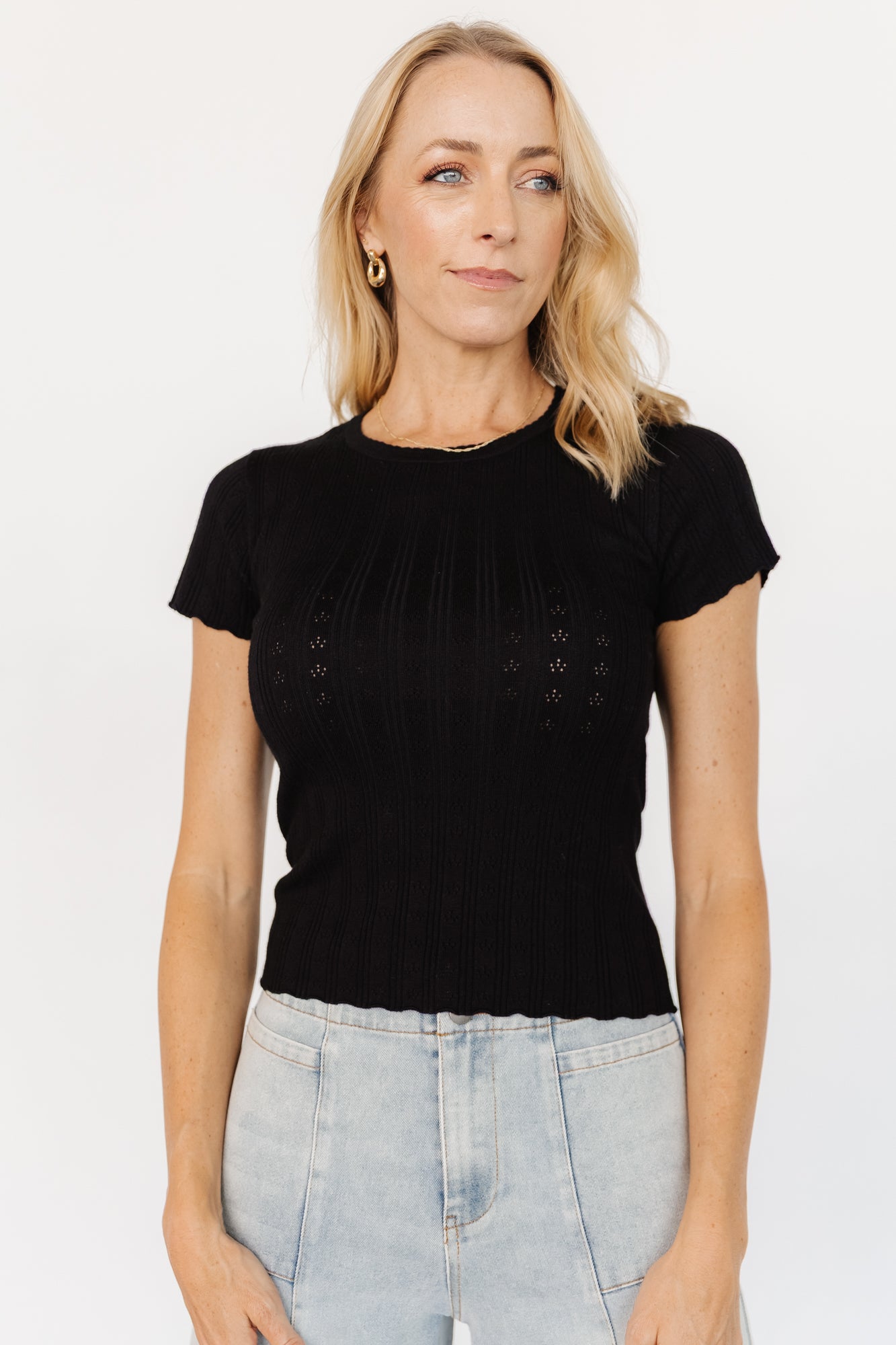 Side view of Penny Pointelle knit top in black showing short sleeve length, curved scalloped hem, and soft drape of the viscose-blend fabric.