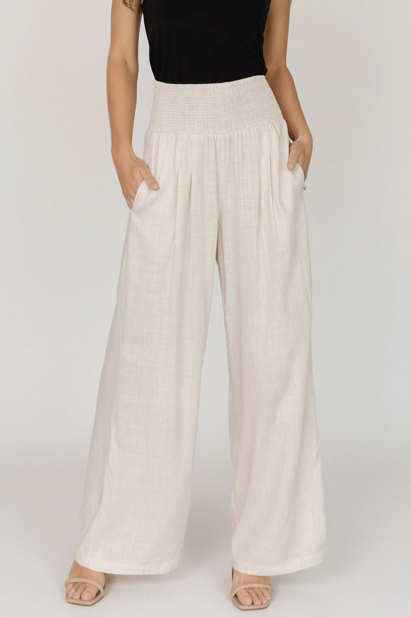 Front view of model wearing Parvati smocked high-waist wide-leg pants in natural linen-rayon blend, showing smocked waist and side pockets.