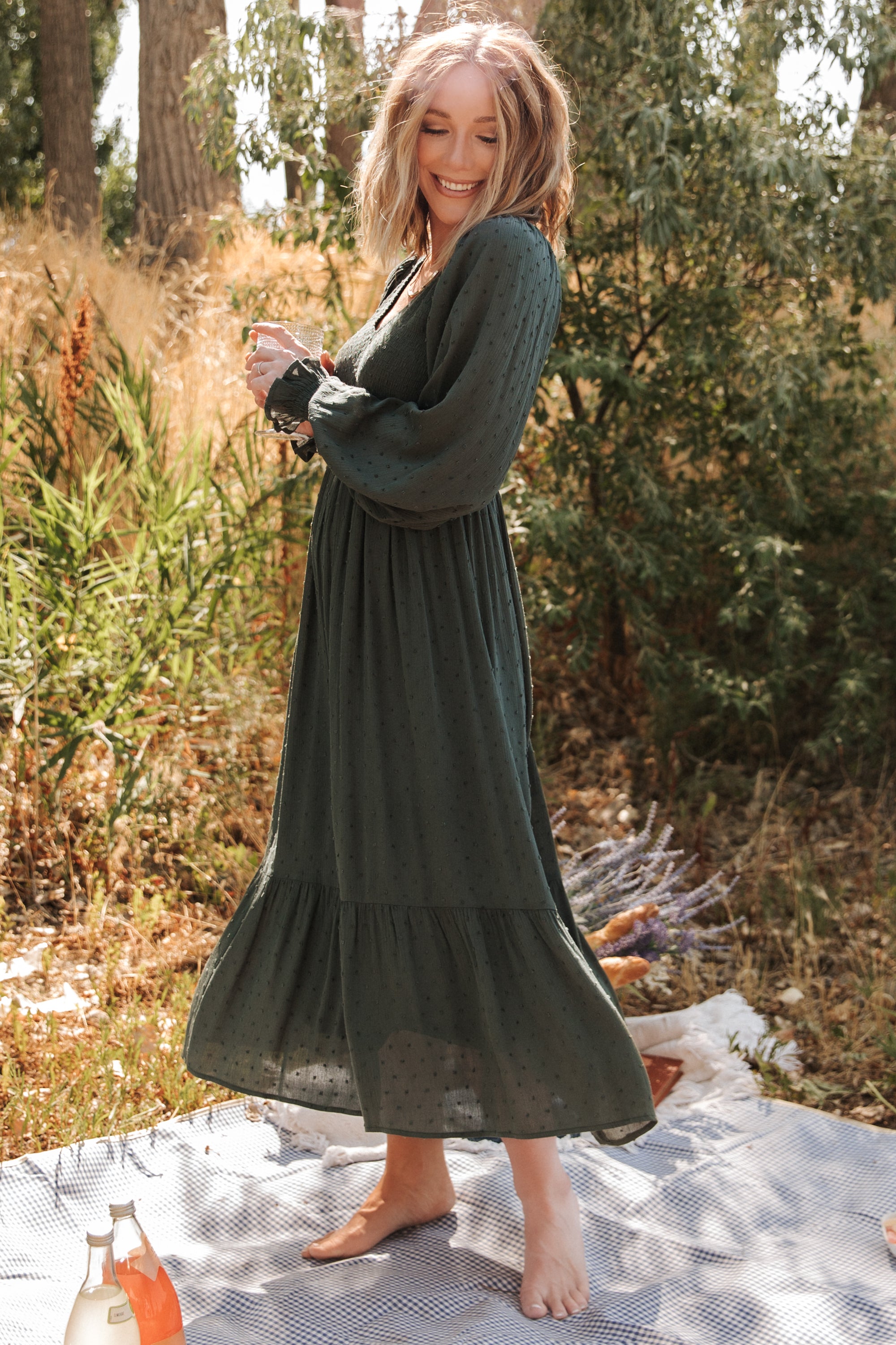 Model walking in a deep olive midi dress with smocked details, illustrating drape and movement of the skirt.
