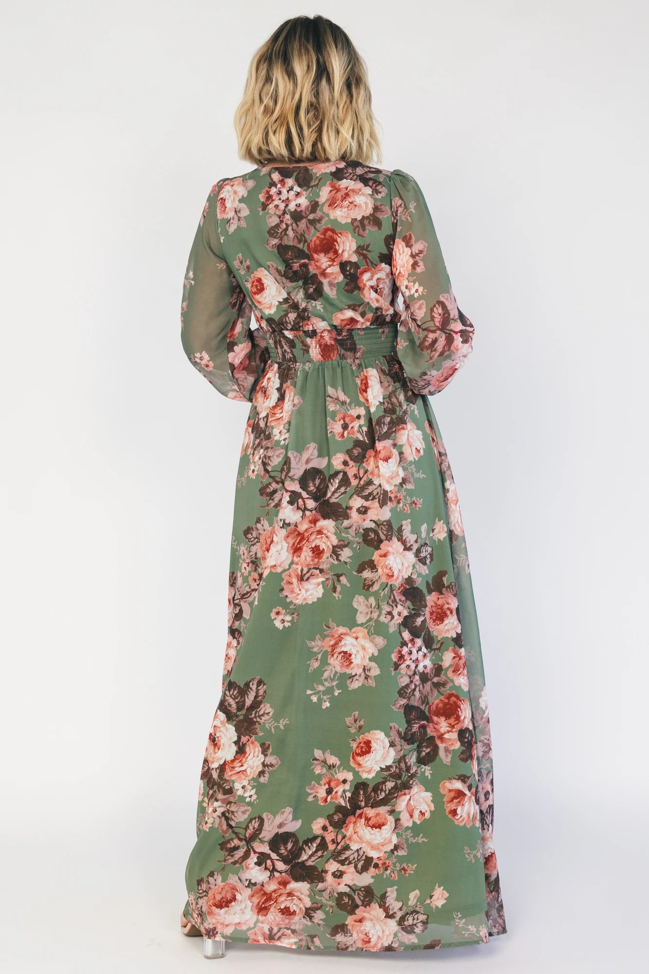 Model wearing a green floral maxi dress with a V-neckline, long bishop sleeves, and a gathered waist with a smocked back.