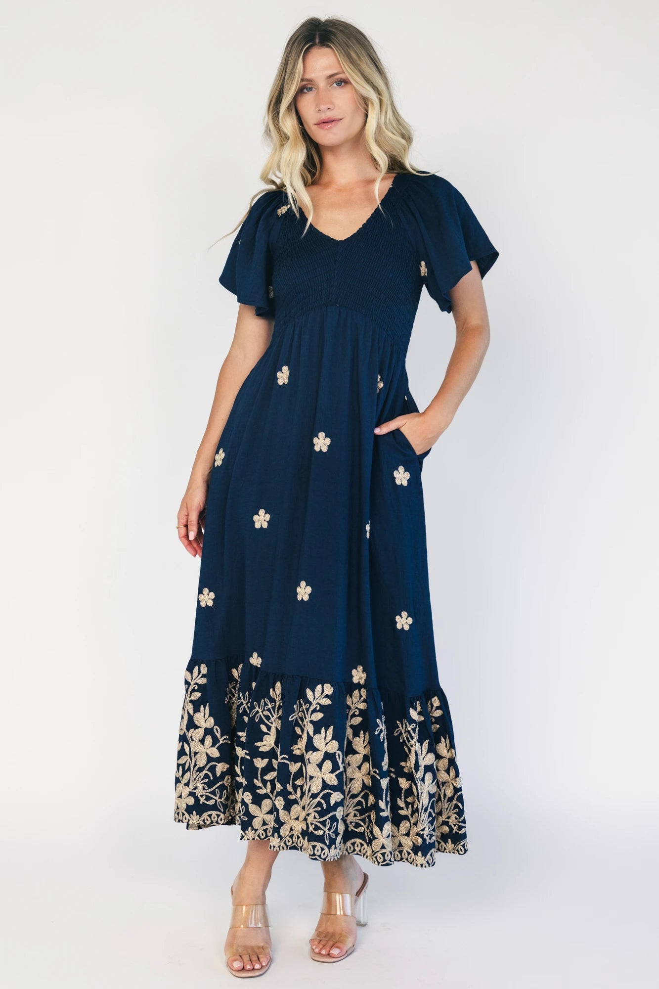 Model wearing a navy embroidered maxi dress with a V-neckline, flutter sleeves, and a smocked bodice.
