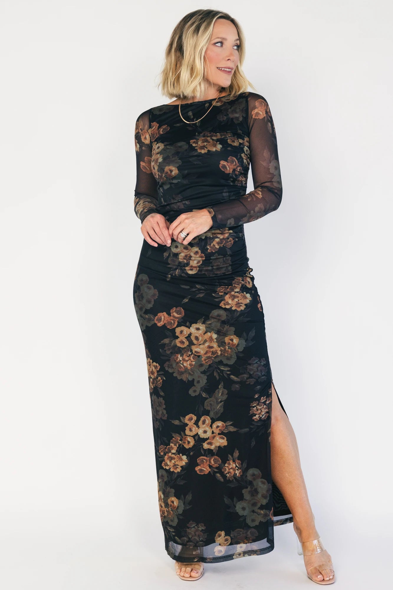 Black mesh bodycon midi dress with muted gold floral print, sheer long sleeves, a round neckline, flattering side ruching, and a thigh-high side slit.