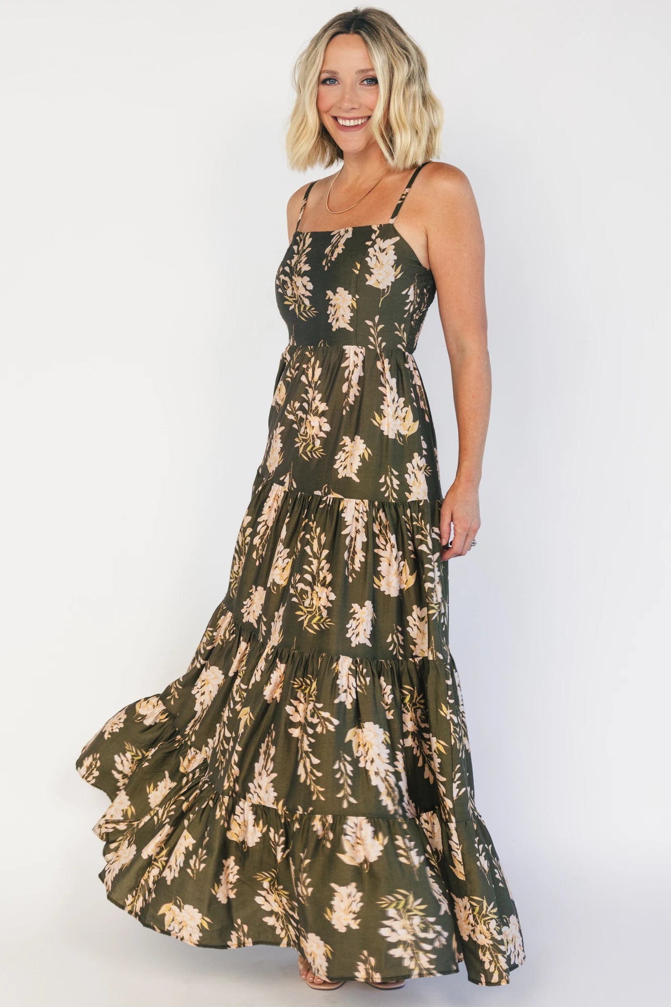 Model wearing an olive floral maxi dress with a square neckline, adjustable spaghetti straps, and a smocked back bodice.