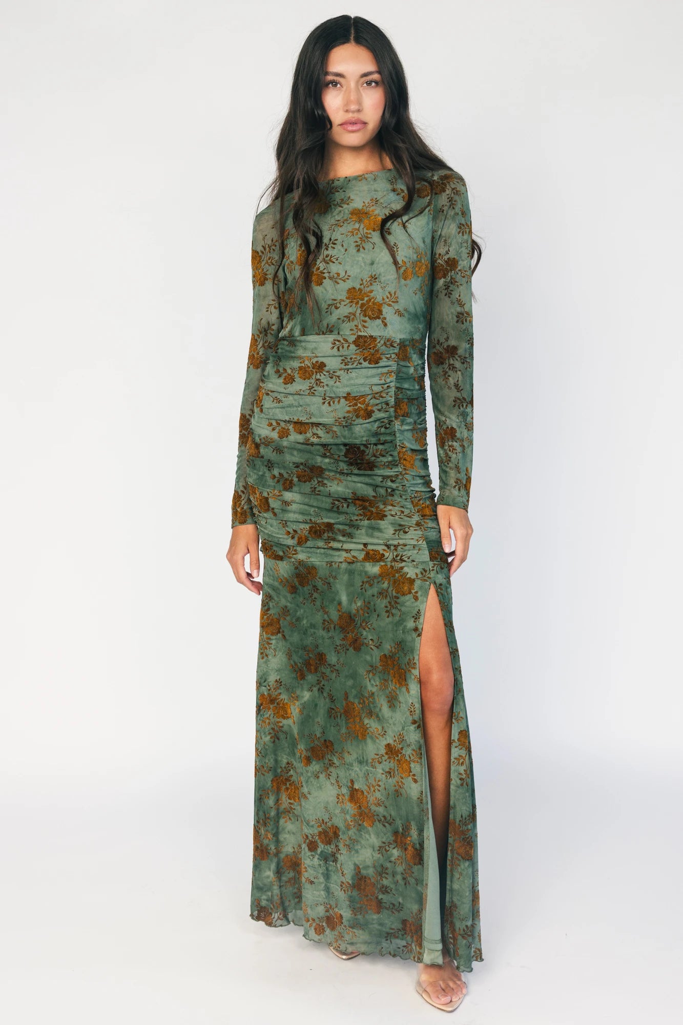 Model wearing a green mesh maxi dress with copper velvet burnout detailing, a high round neckline, and long sheer sleeves.