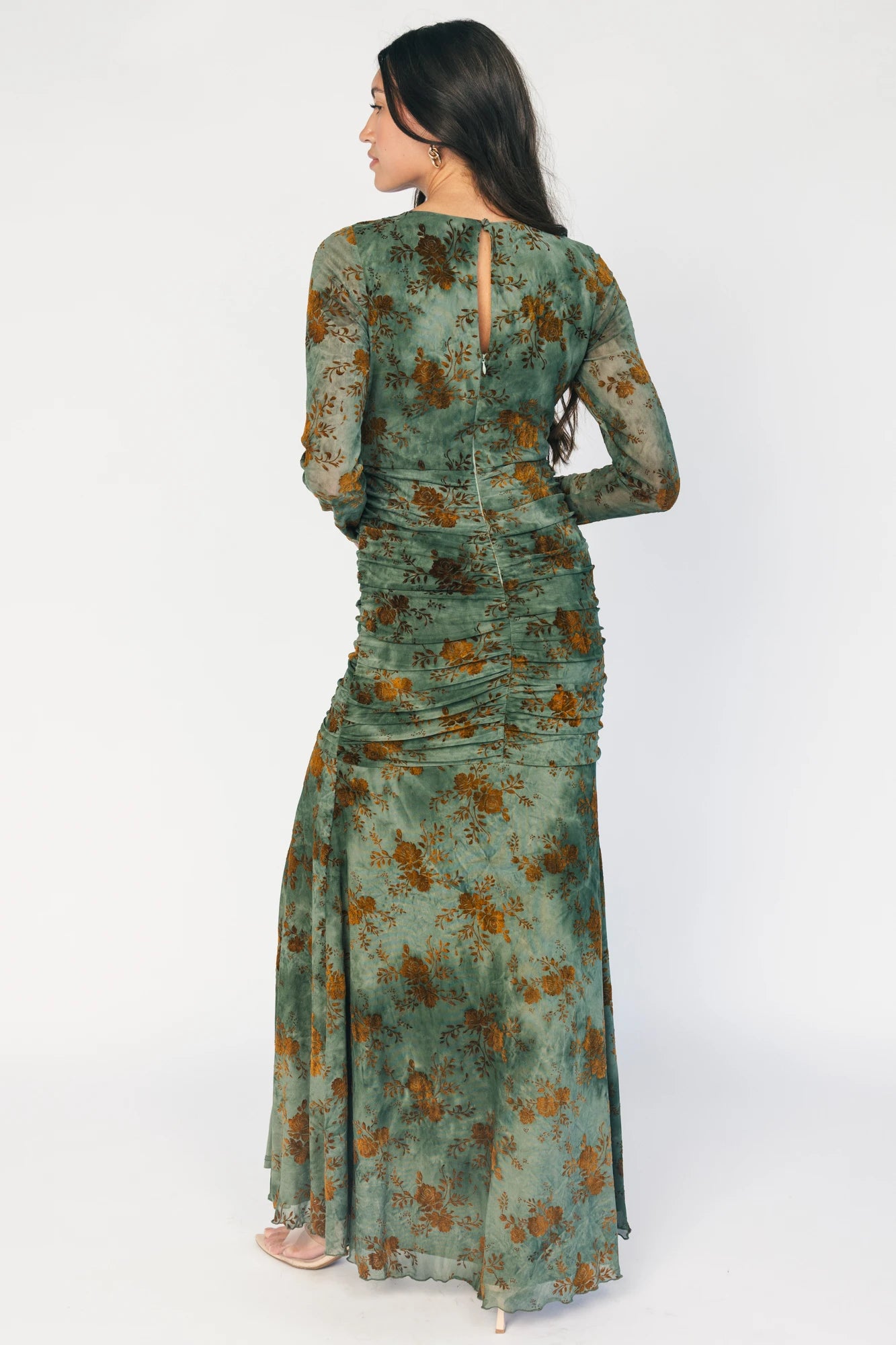 Model wearing a green mesh maxi dress with copper velvet burnout detailing, a high round neckline, and long sheer sleeves.