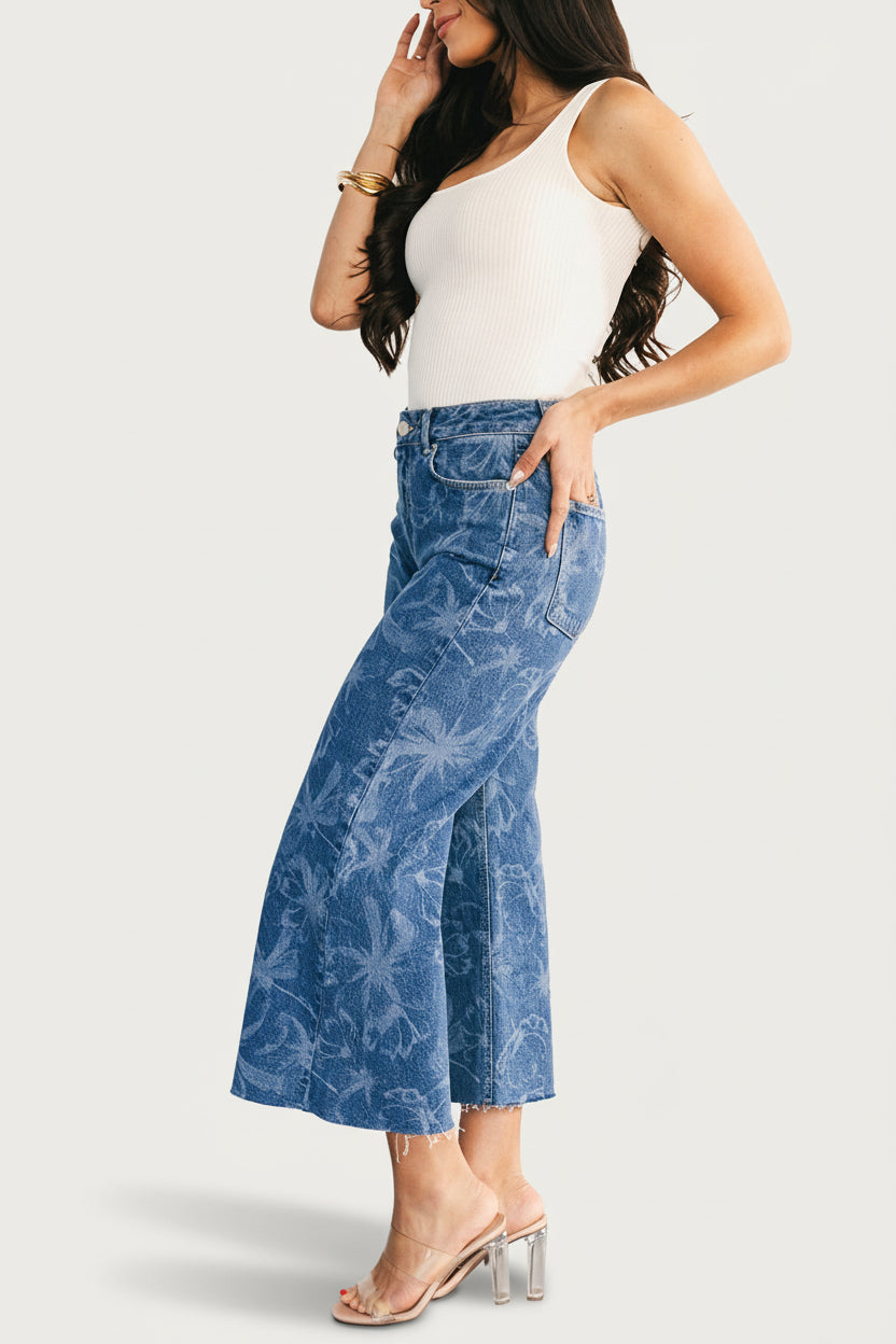 Flat-lay of medium floral wash Cádiz jeans showing full laser-printed pattern, cropped straight leg, and raw hem (approx. 96 chars)