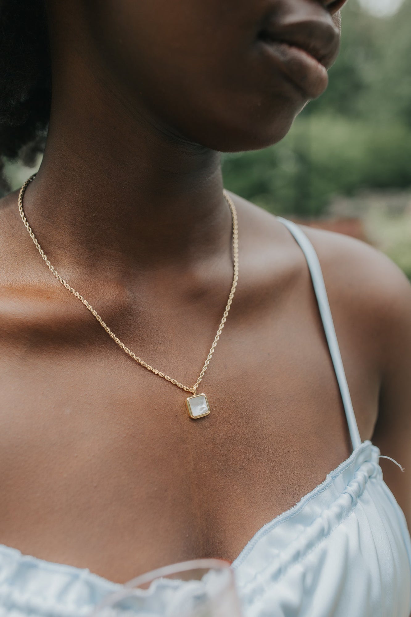 Mother of Pearl Broadwater necklace displayed on a neutral surface, highlighting the iridescent square stone and the warm 18K gold-plated finish of the chain.