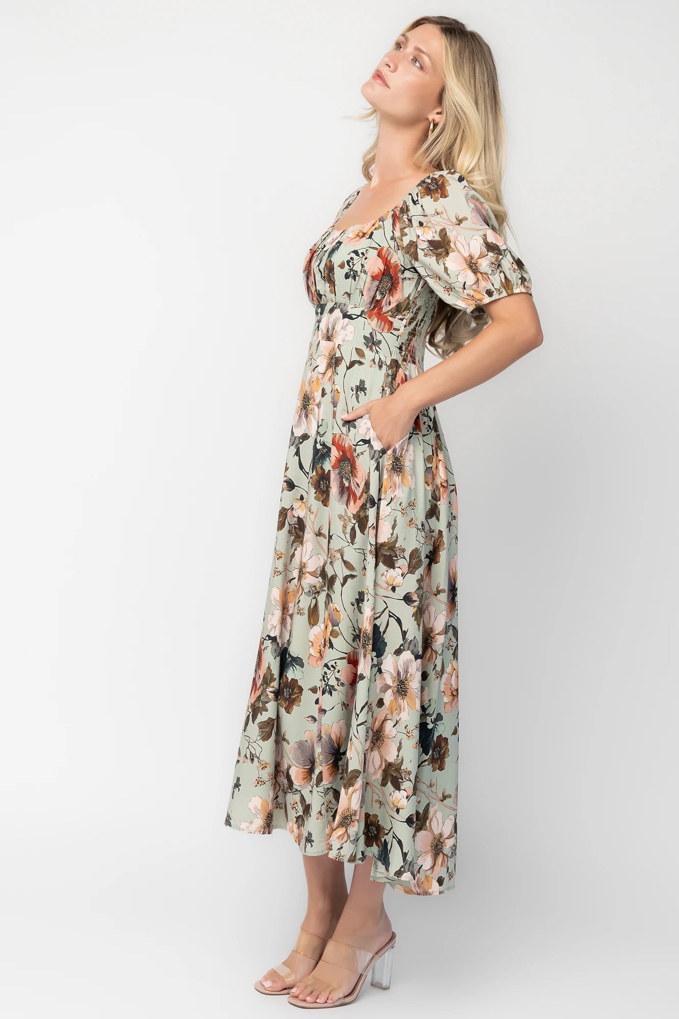 Model wearing the Charlotte Midi Dress in Sage, a sage green midi dress with a pink multi floral print, rounded square neckline, puff sleeves, banded waist, and flowing A-line skirt with side pockets.