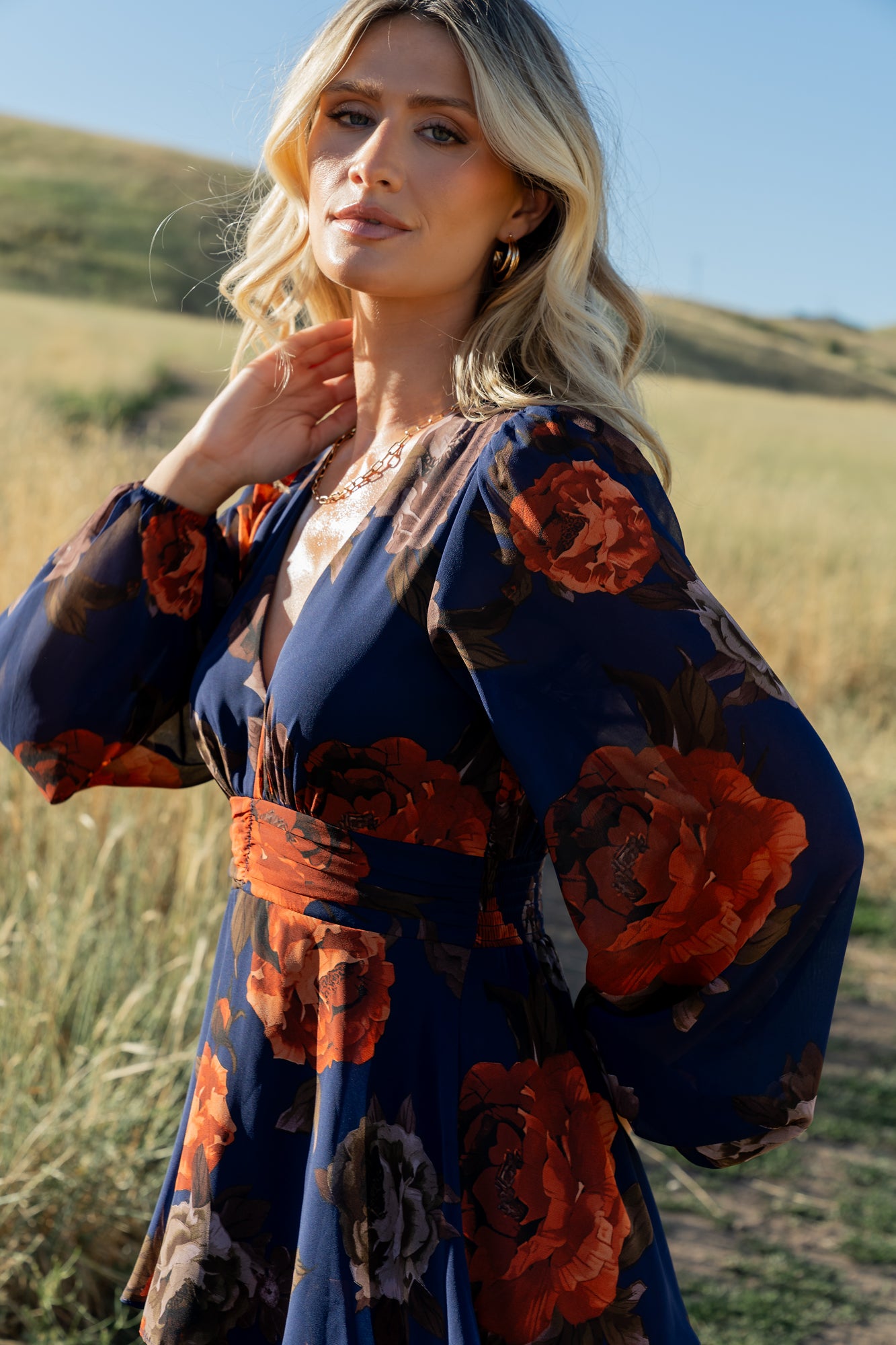 Lifestyle image of Mariella dress styled for a wedding guest look, showing navy + rust floral chiffon, V-neck, and flowing tiered skirt.