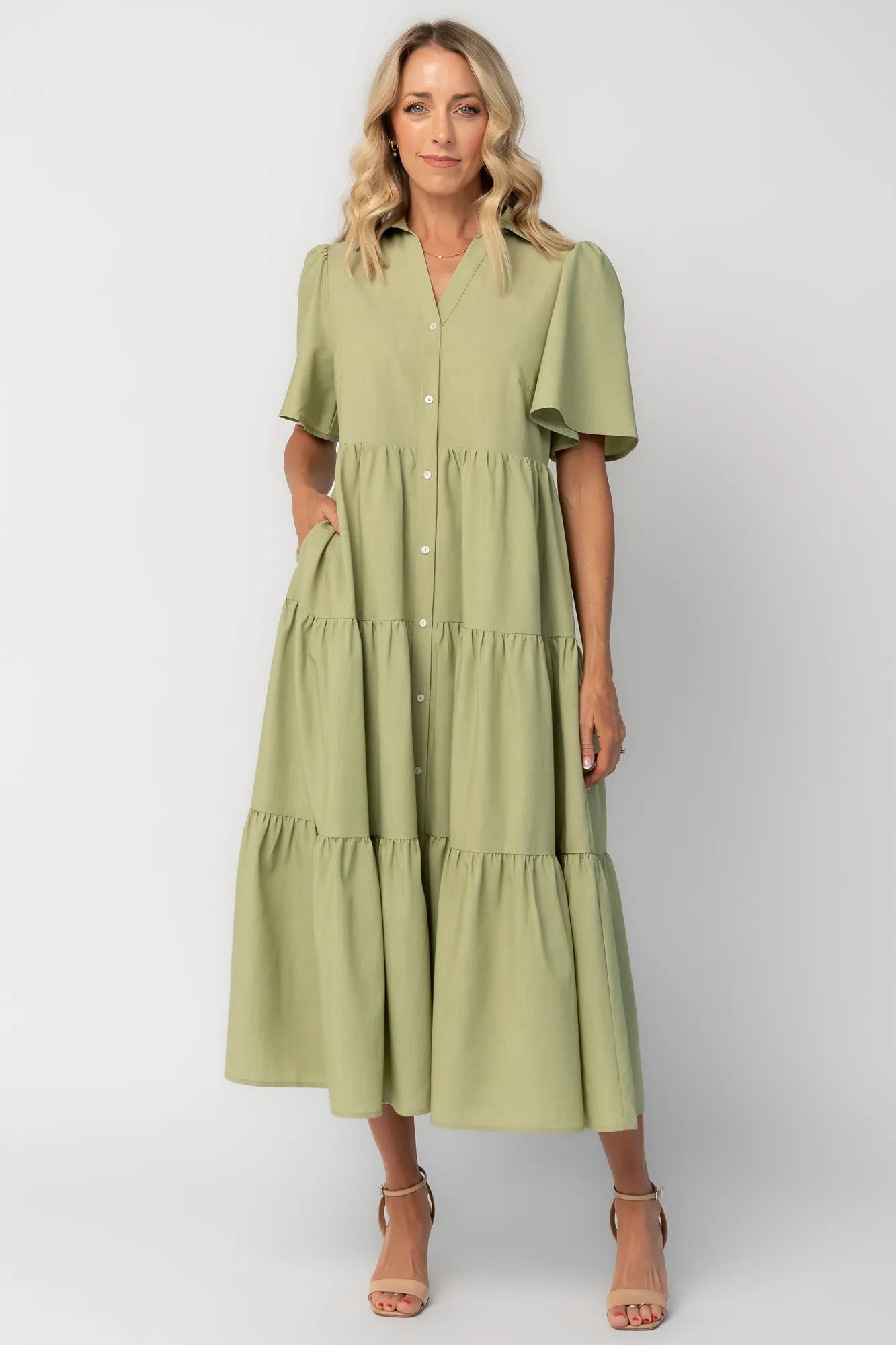 Model wearing a sage green midi dress with a collared neckline, button-front bodice, and short flutter sleeves.
