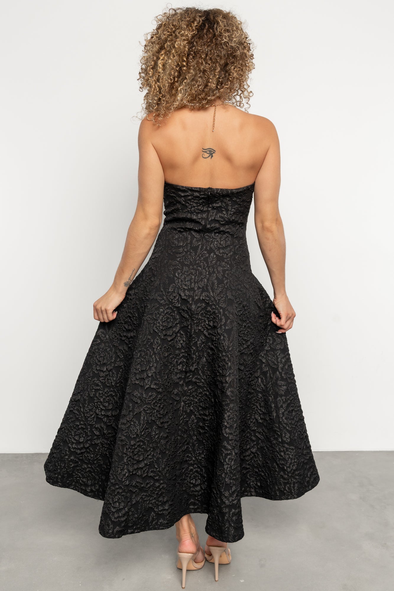 Rear view showing Selene's hidden back zipper and smooth full lining on a black strapless midi dress with textured floral motif.