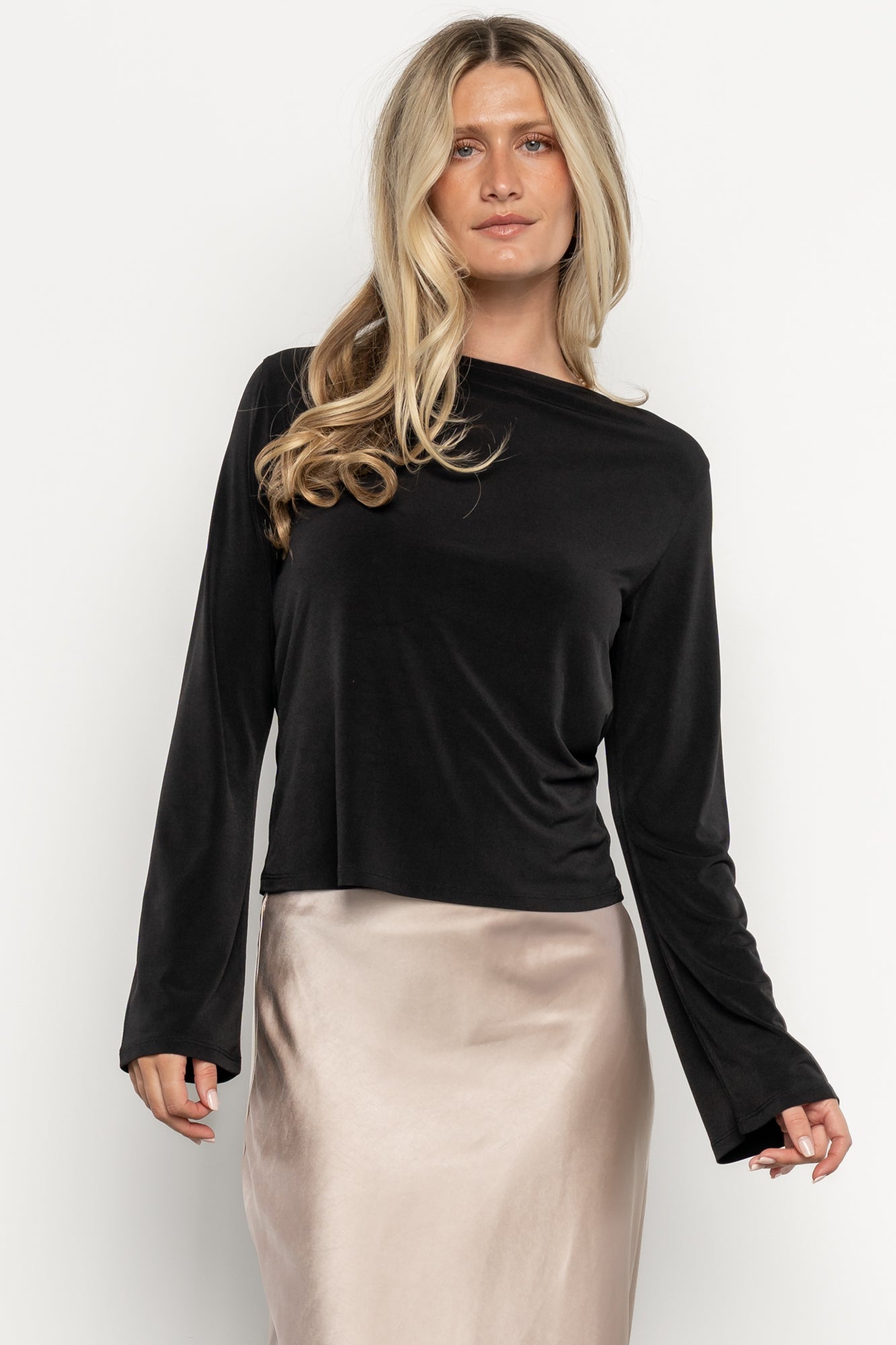 Front view of the Tasia Drape Back Top in black on a model, showing boat neckline, long bell sleeves and lightweight luxe knit drape.