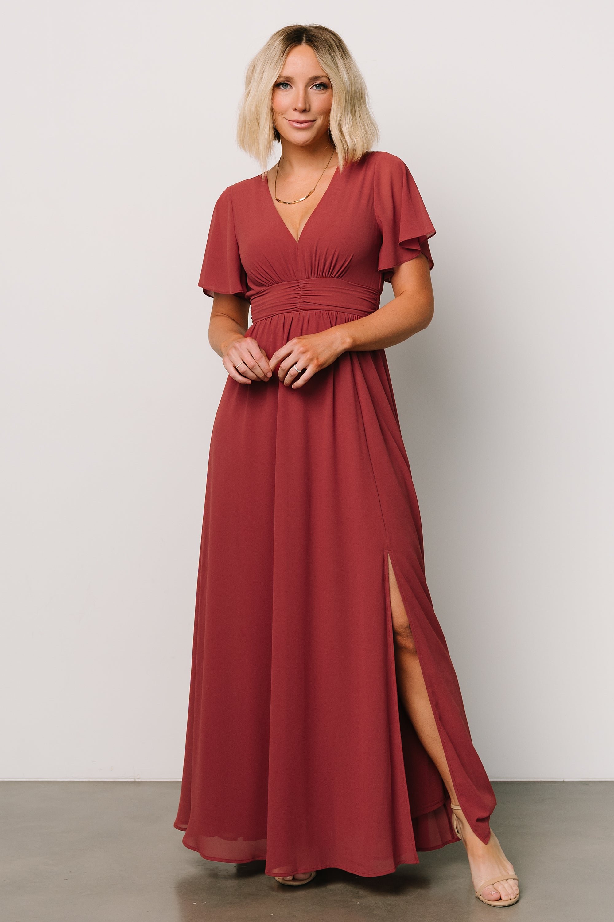 Front view of terracotta Ramona maxi dress hanging on a mannequin, highlighting flutter sleeves and ruched empire waist.