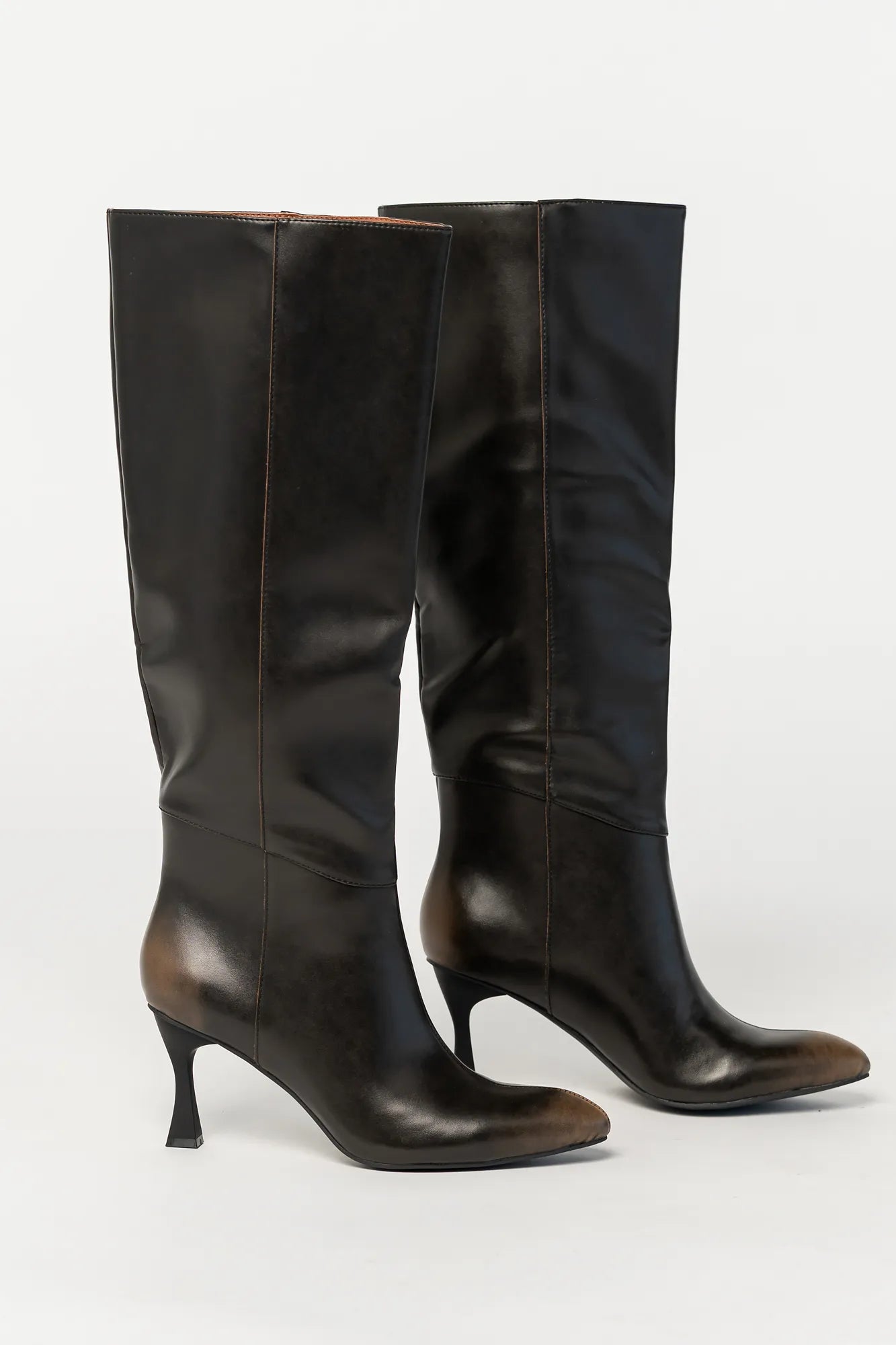 Pair of black knee-high boots featuring a pointed toe, sleek fitted shaft, and sculpted kitten heel. The streamlined silhouette and smooth finish create an elegant, versatile look that pairs effortlessly with dresses, skirts, and tailored outfits.