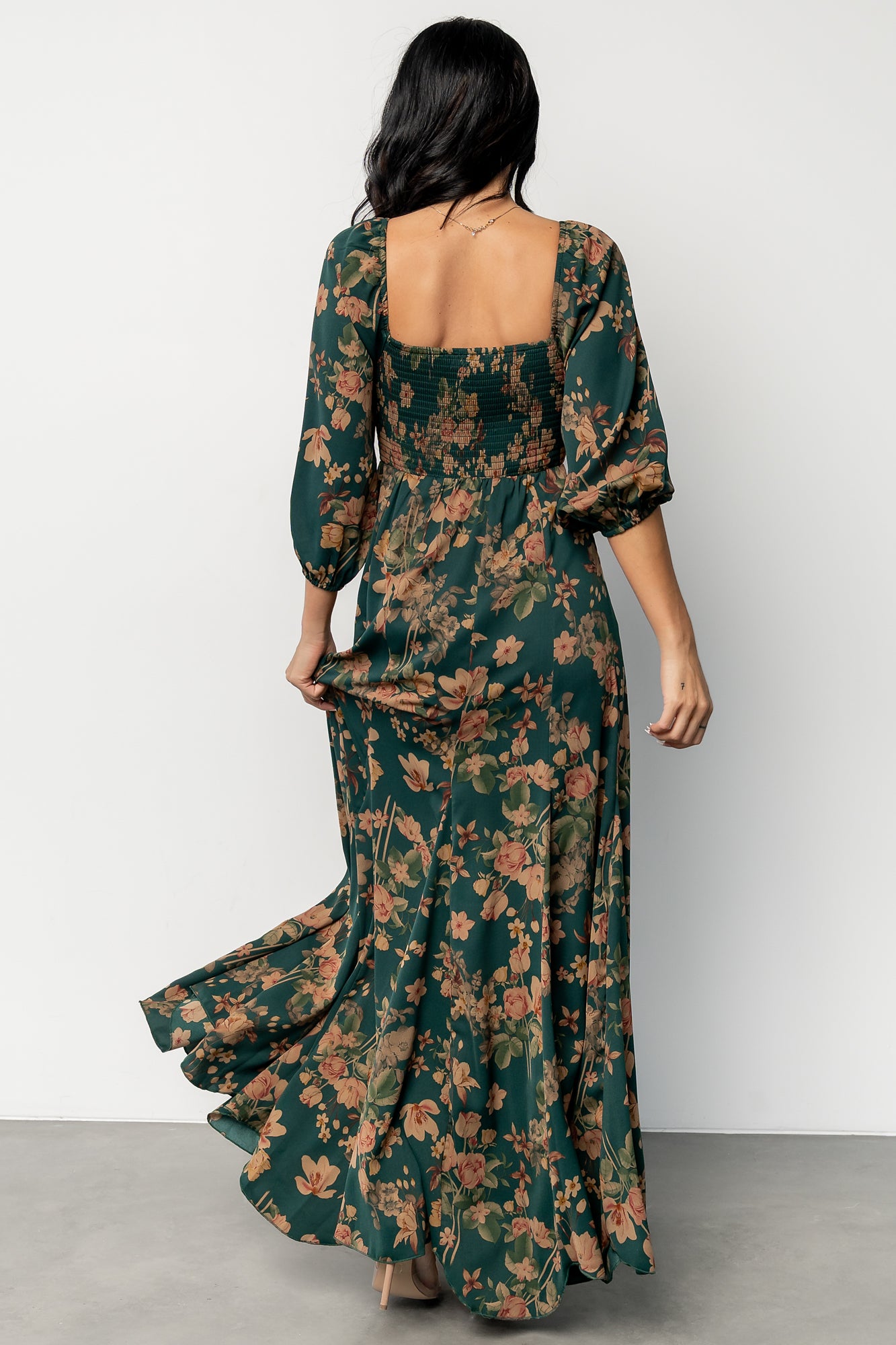 Model wearing green and copper floral maxi dress walking to show godet hem flare and hemline length.