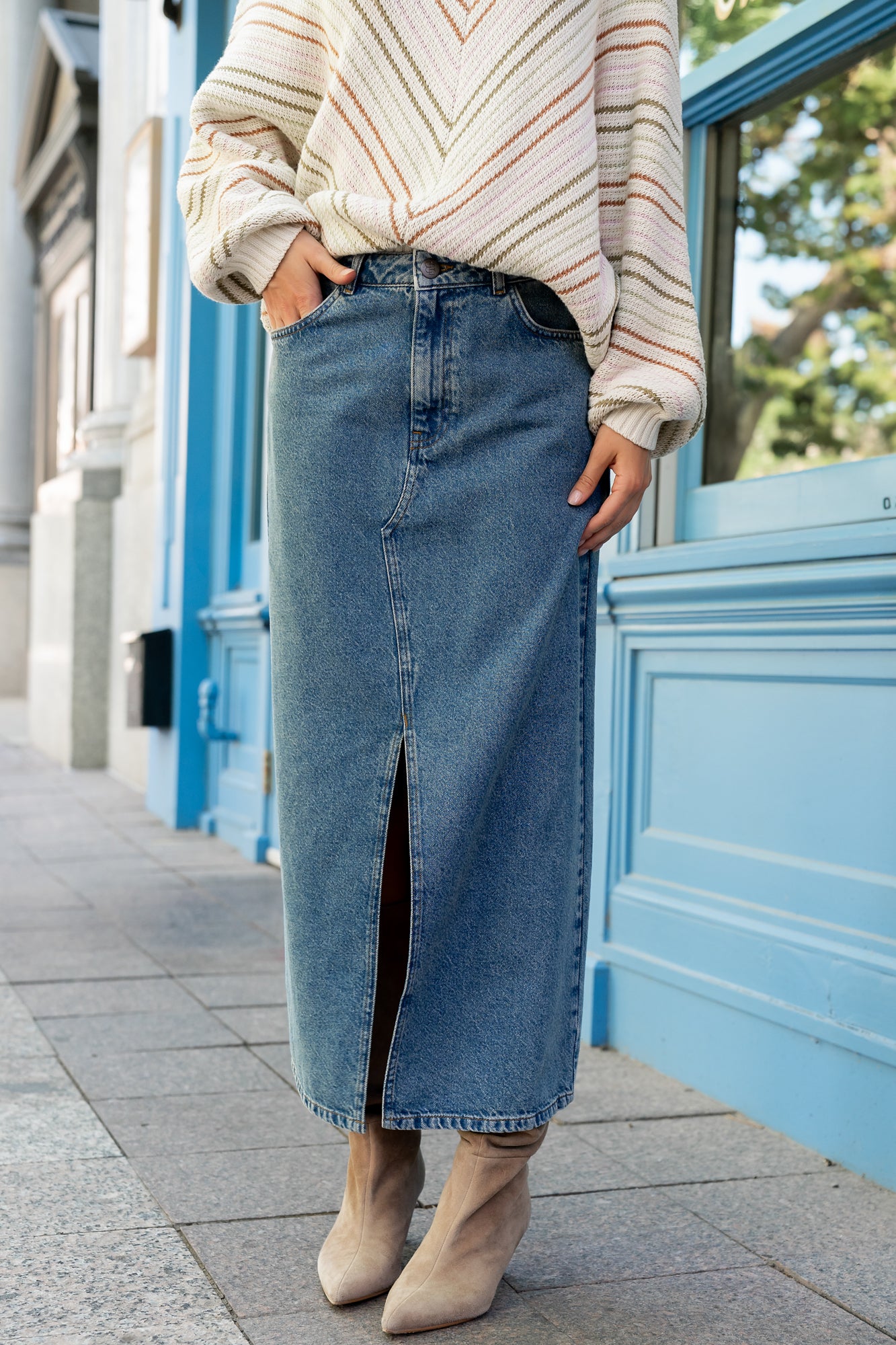 Side profile of Aleksa medium wash denim midi skirt highlighting center-front slit, mustard topstitching, and clean silhouette.