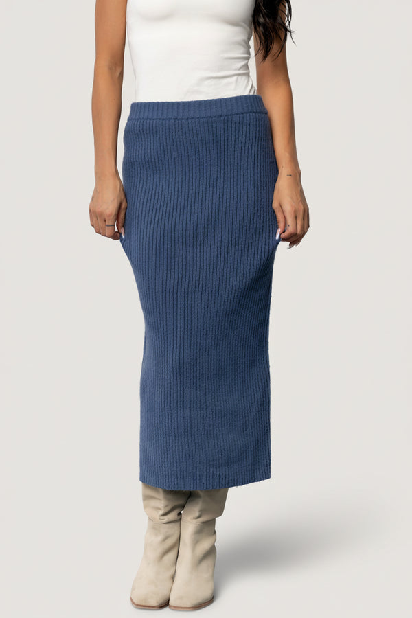 Front view of the blue Blair rib knit midi skirt on model, fitted through the hips with a raw hem and a stretchy elastic waistband for comfort.