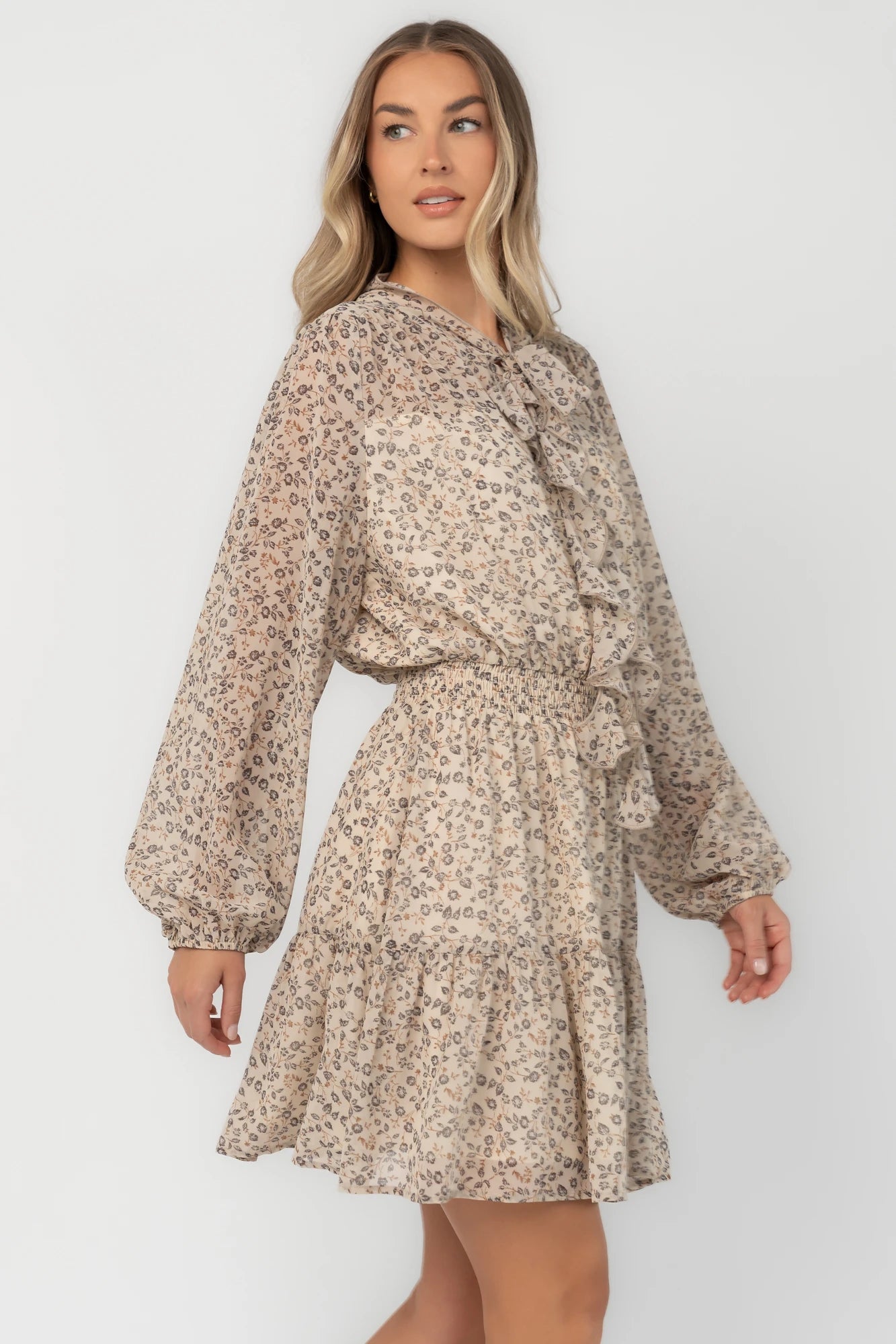 Cream floral mini dress with a self-tie neckline, cascading ruffle detail, long balloon sleeves, smocked waist, and tiered skirt.