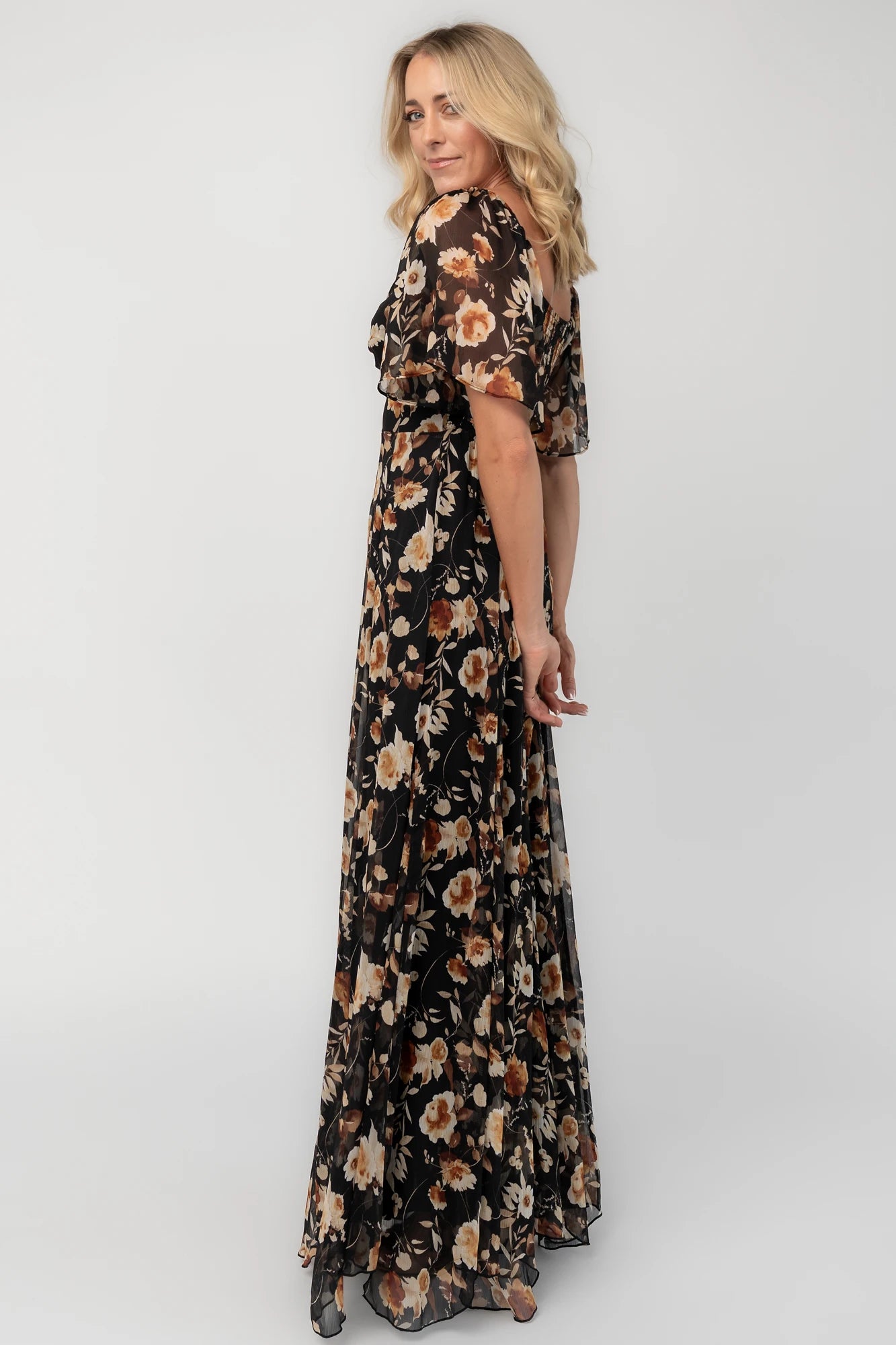 Black floral chiffon maxi dress with a sweetheart neckline, flutter sleeves, smocked back bodice, tiered skirt, and subtle gold foil detailing.