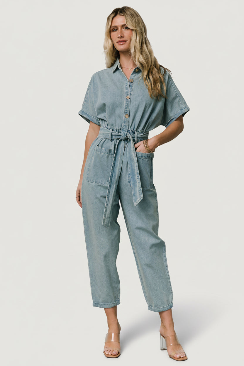 Back view of Mateo jumpsuit showing back patch pockets, tapered cuffed pant leg, and washed denim texture on model.