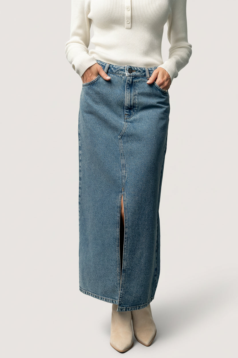 Model wearing Aleksa denim midi skirt styled with a sweater and booties, showing midi length, slit movement, and everyday styling.