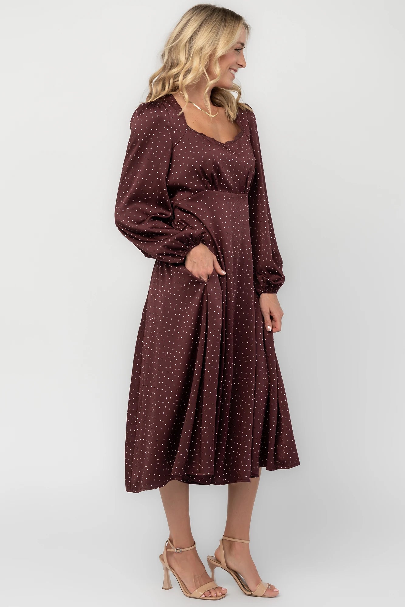 Mahogany brown midi dress with a square neckline, long sleeves, smocked back waist, removable back bow, side pockets, and a flowing skirt with heart details.