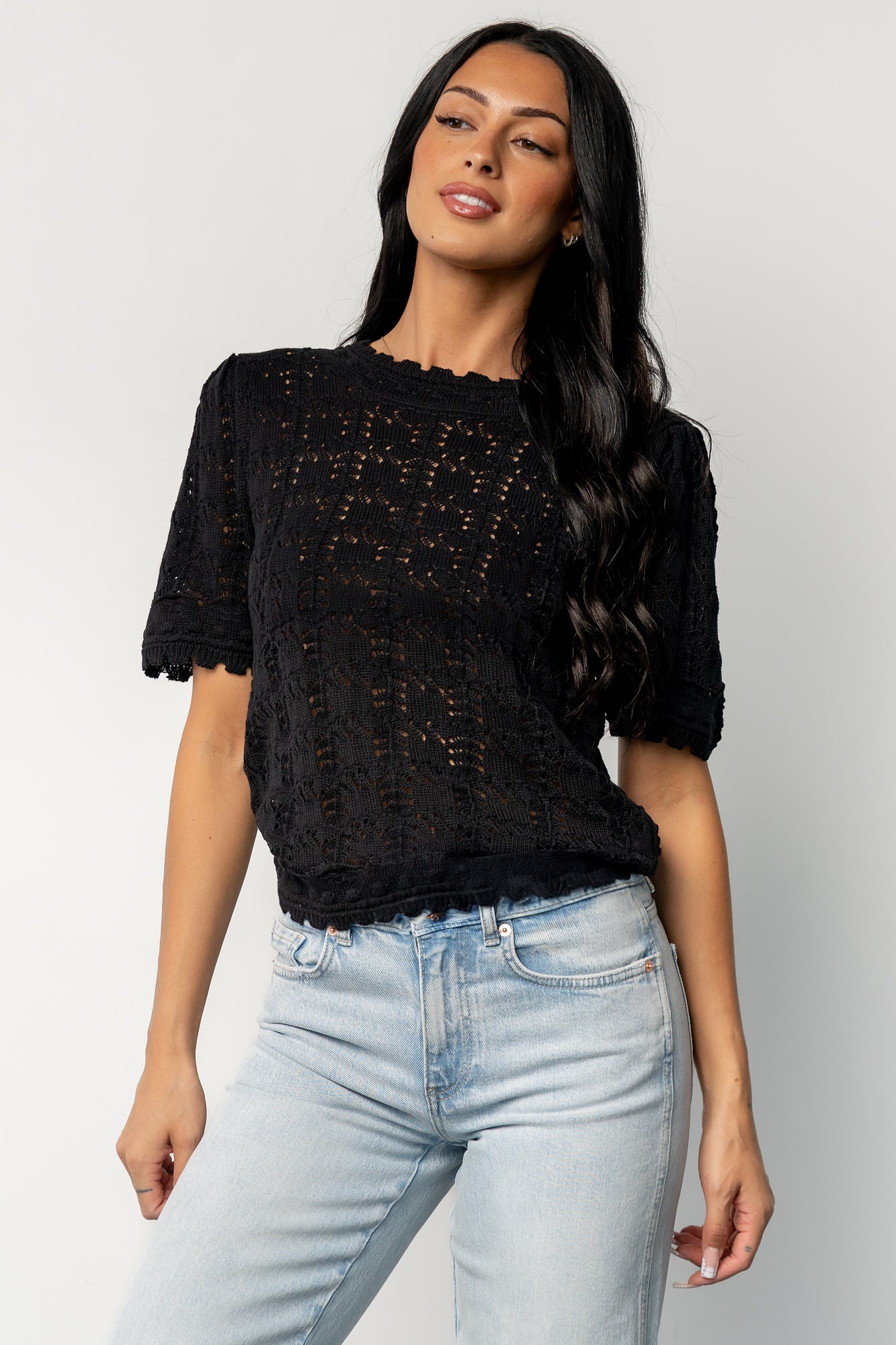 Side profile of the Serenity Knit Sweater Top in black on a model, highlighting scalloped sleeve edge, slight stretch knit, and textured crochet pattern.