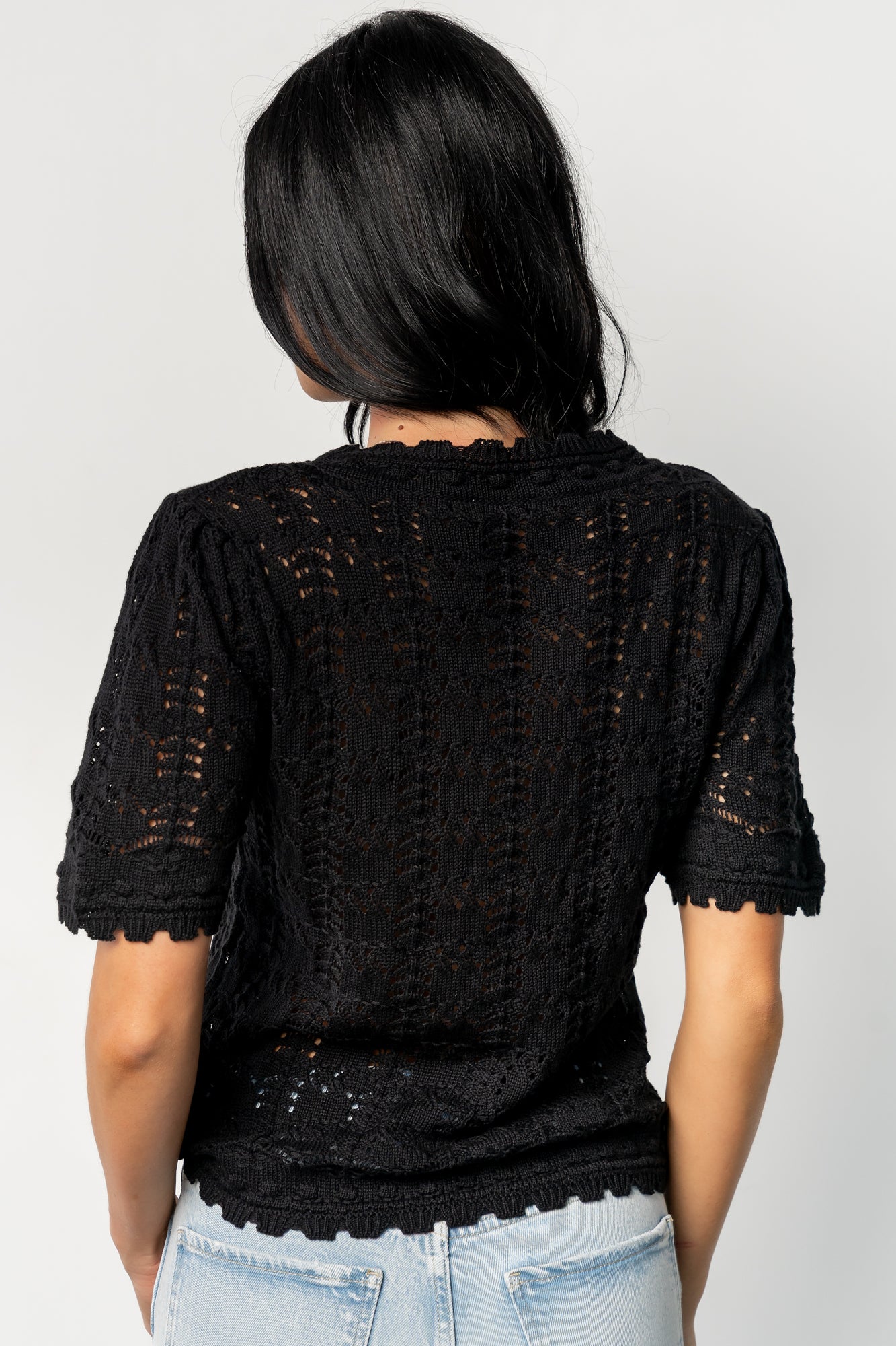 Close-up detail of scalloped collar and open-knit crochet holes on the Serenity Knit Sweater Top in black, showing yarn texture and stitch pattern.