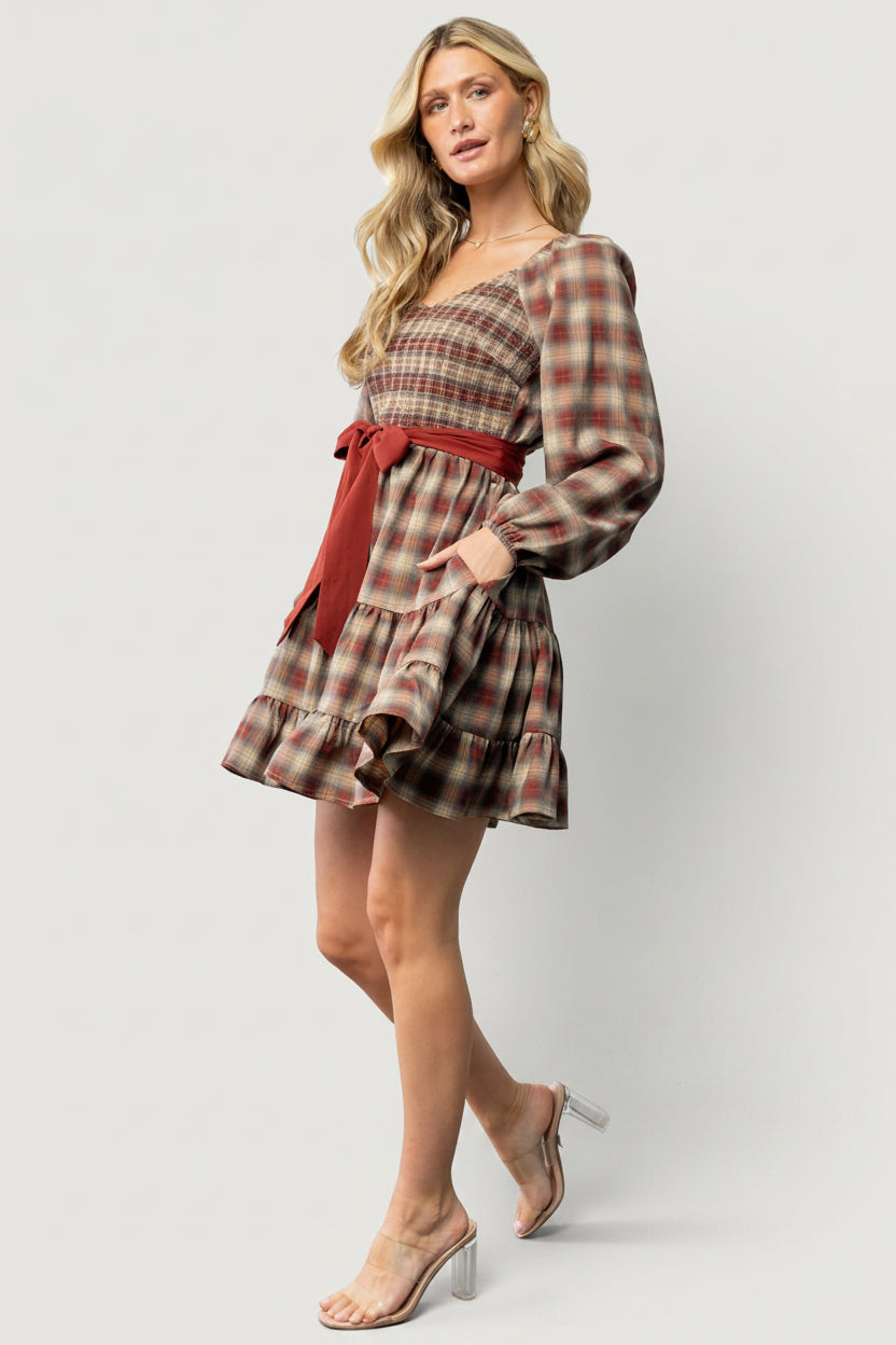 Close-up of Stina dress fabric and smocked bodice showing plaid colors—rust, orange, yellow, and gray—and textural detail.
