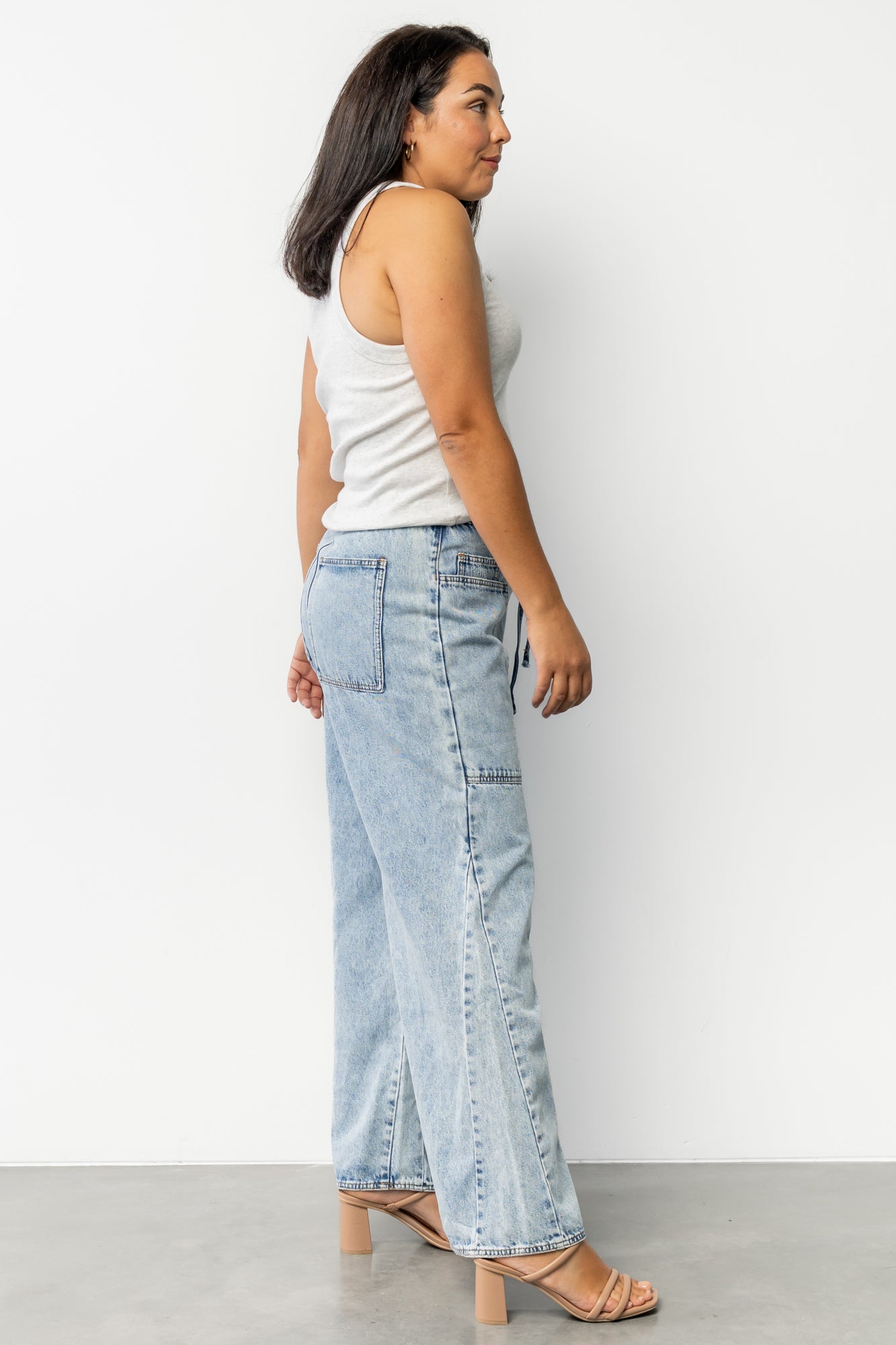 Close-up of split outseam and hem detail on light wash jeans, highlighting finishing, stitches, and modern raw-edge styling.