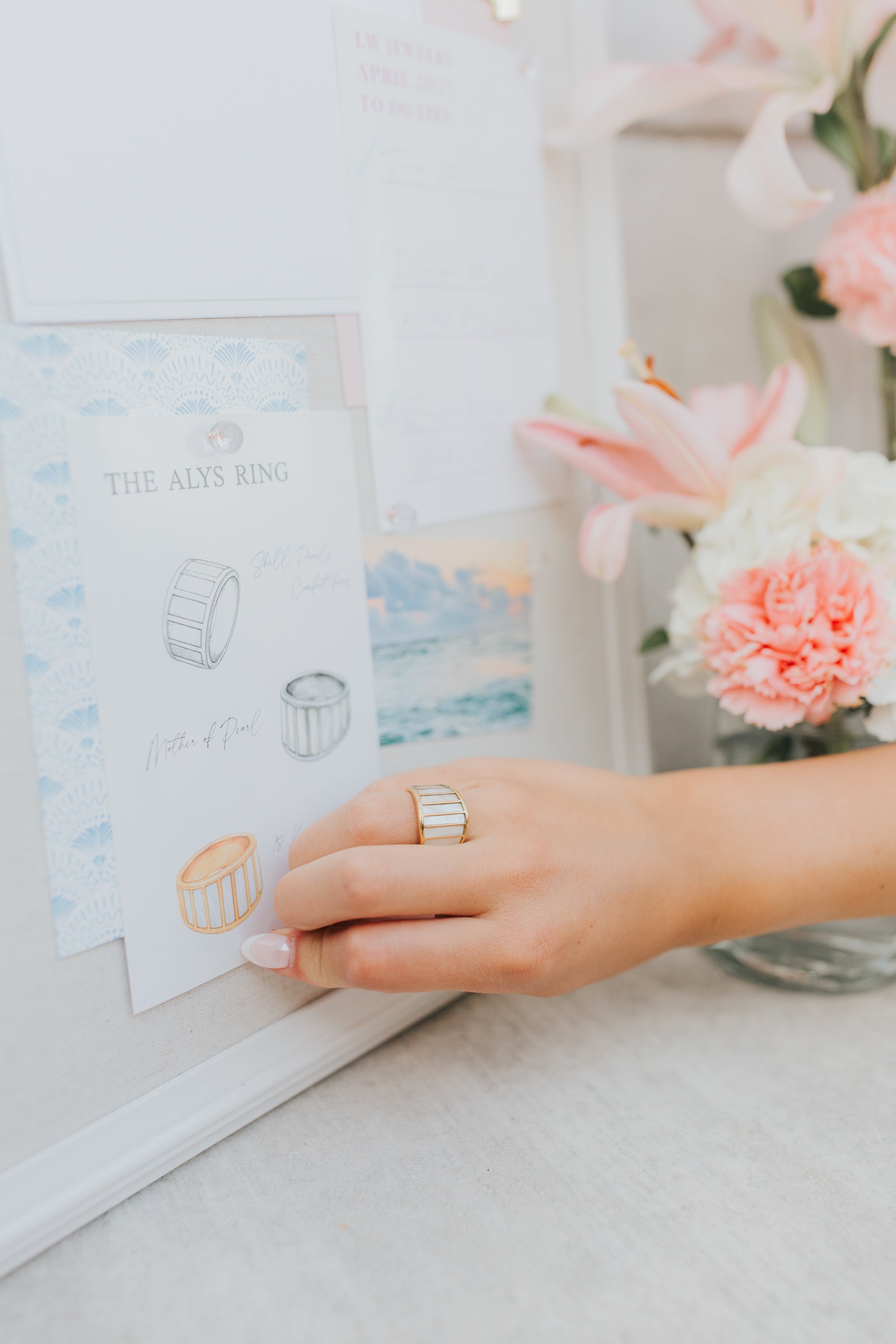 Styled still-life of the Alys ring next to simple jewelry pieces, highlighting its modern profile and reflective gold-tone finish.