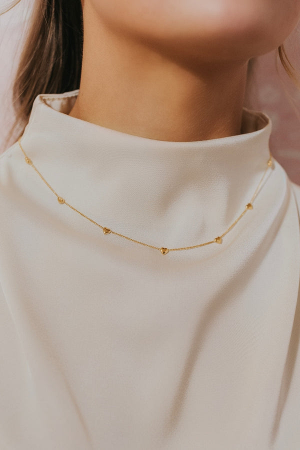 Close-up of gold-plated little hearts necklace laid flat on a white background, showing linked heart charms, polished finish, and clasp detail.