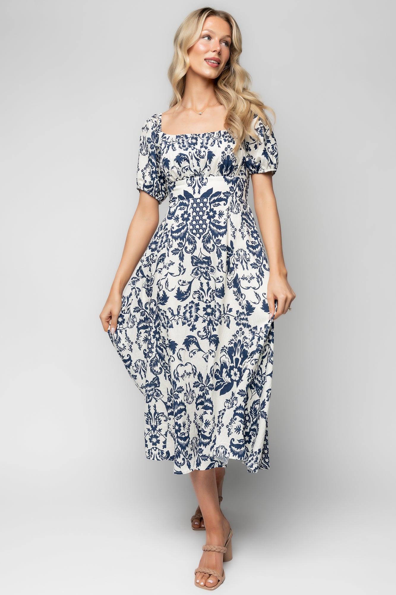 Full-length pose of the ivory and dark blue floral midi dress on model, highlighting banded waist, oversized sleeves, and soft drape of the fabric.