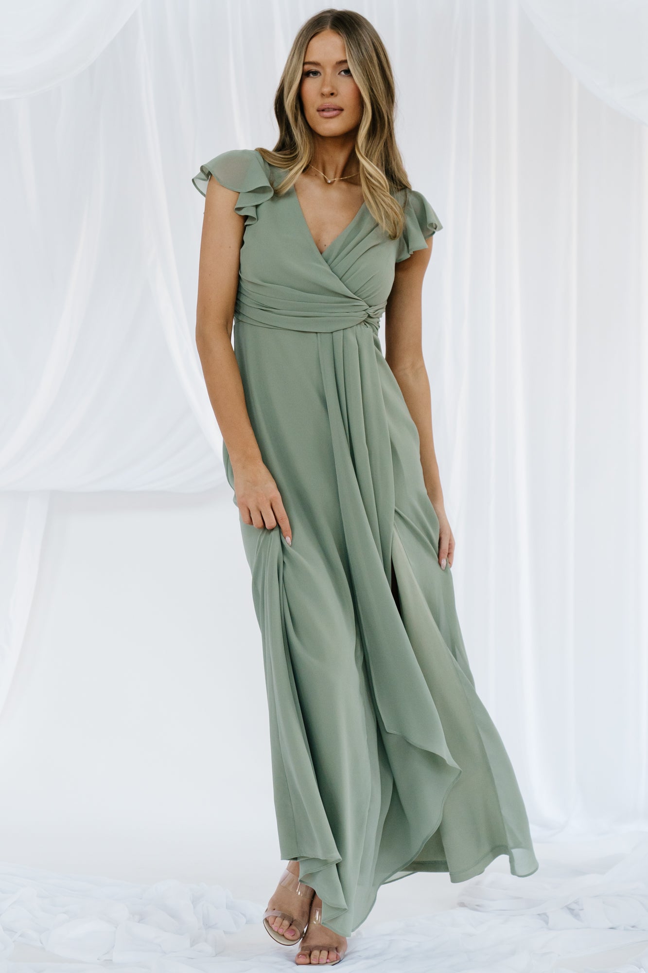 Full-length front view of dusty green Jasmine chiffon maxi dress on model, showing crossover V-neck, faux knot, flutter sleeves, and flowing skirt.
