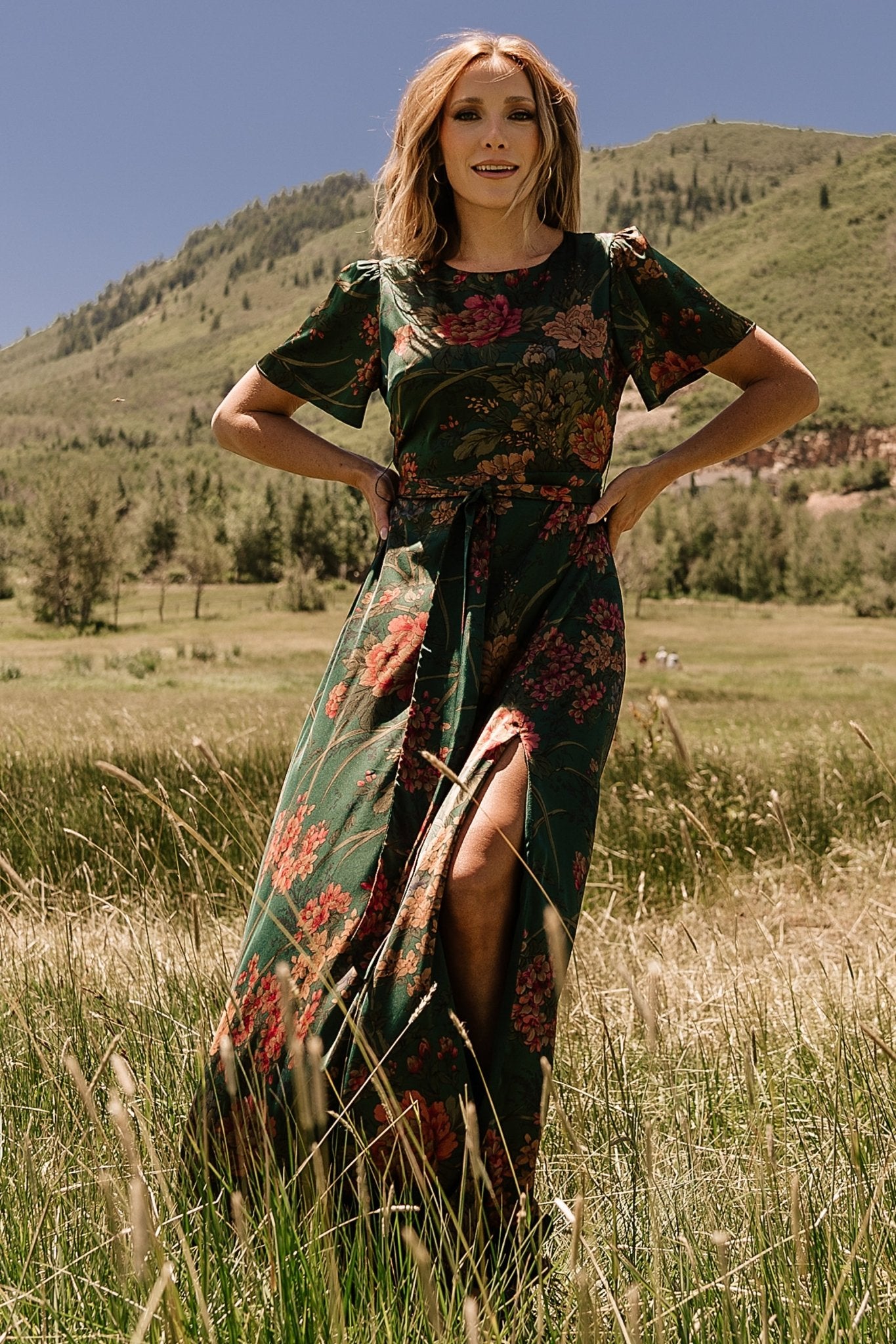 Detail view of removable waist tie and belt loops on dark green floral satin maxi dress, tied at the natural waist.