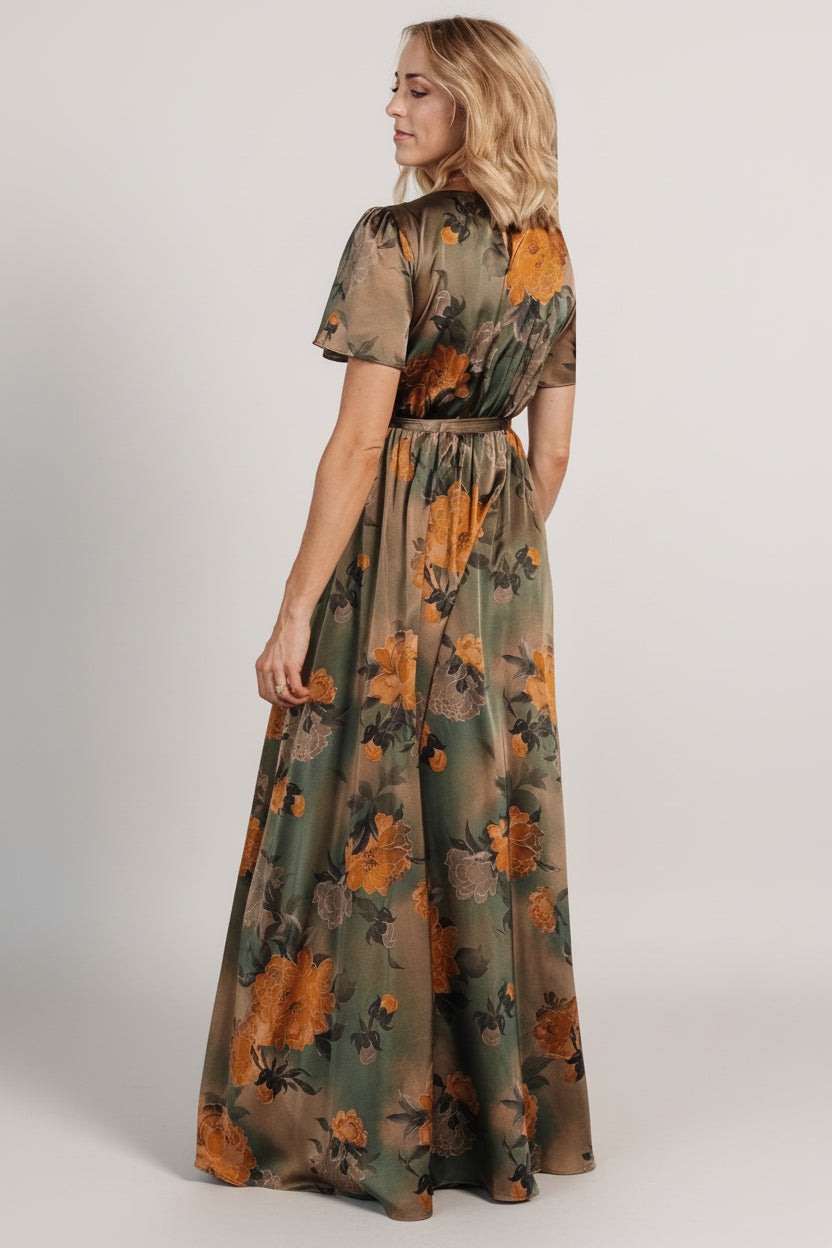 Side angle of olive floral satin maxi dress showcasing the left-leg slit and fluid movement of the skirt while walking.