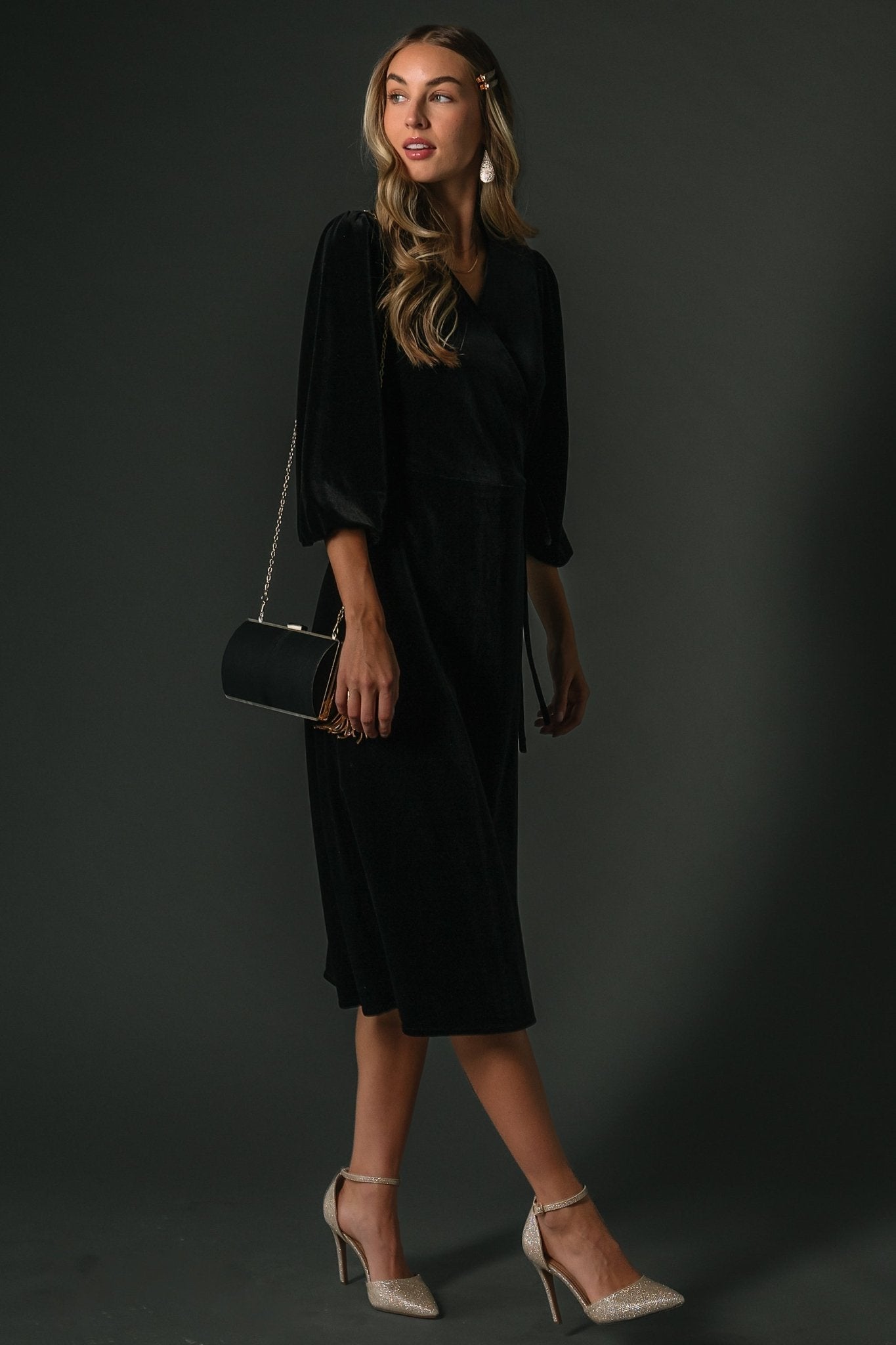 Studio shot of black velvet wrap dress on mannequin highlighting true wrap V-neckline and midi hemline silhouette.