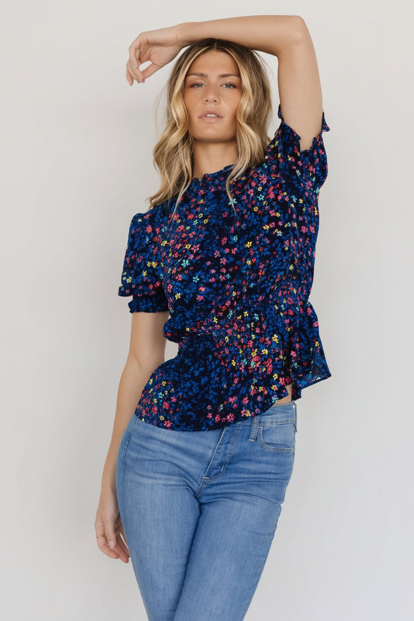 Model wearing the Blue Multi Beth Peplum Top in size S, showing fit at bust, defined smocked waist, and short ruffled sleeves.