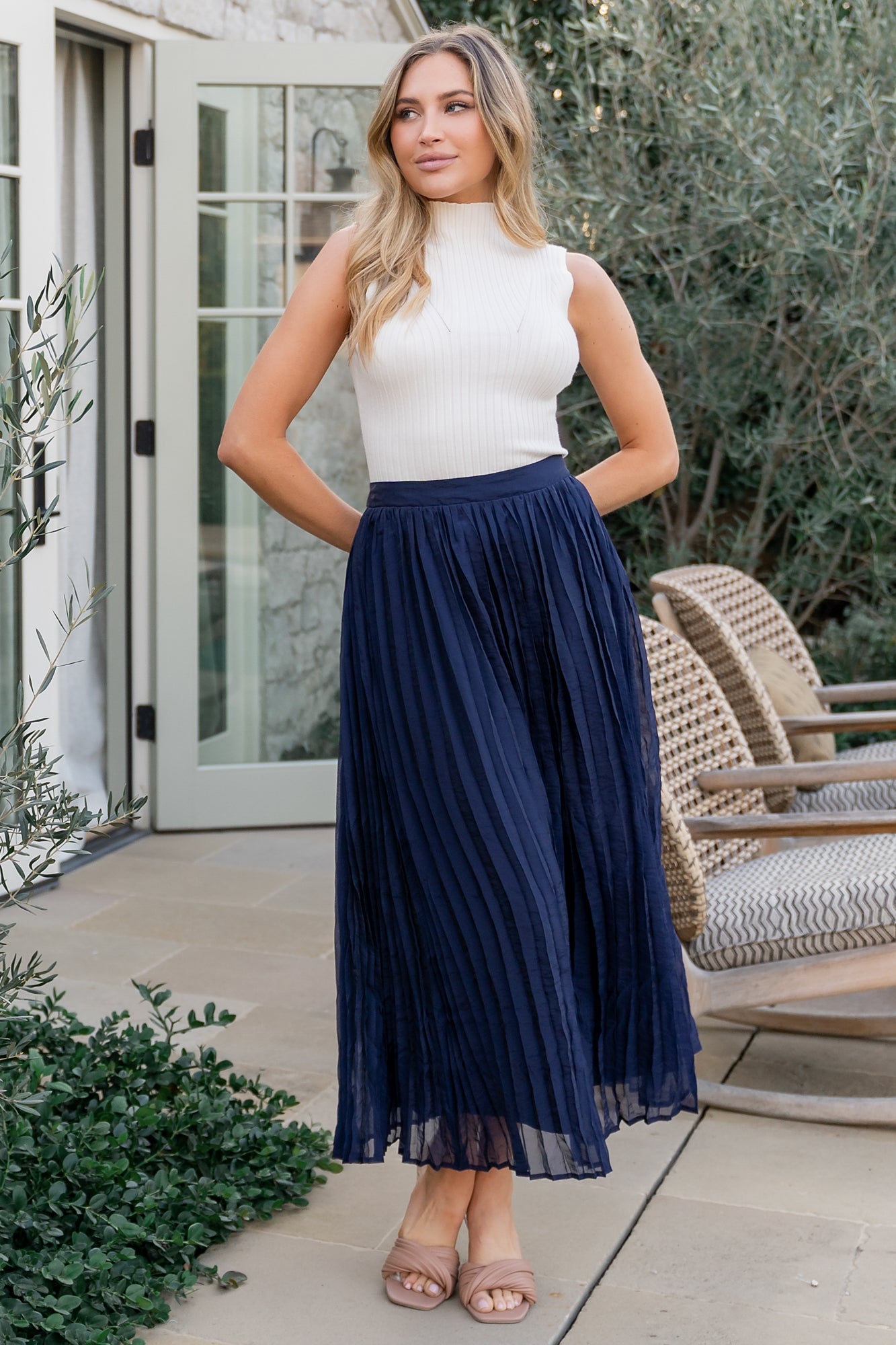 Three-quarter shot of navy pleated midi skirt highlighting pleat texture, midi hemline, and lightweight organza-like fabric flow in motion.