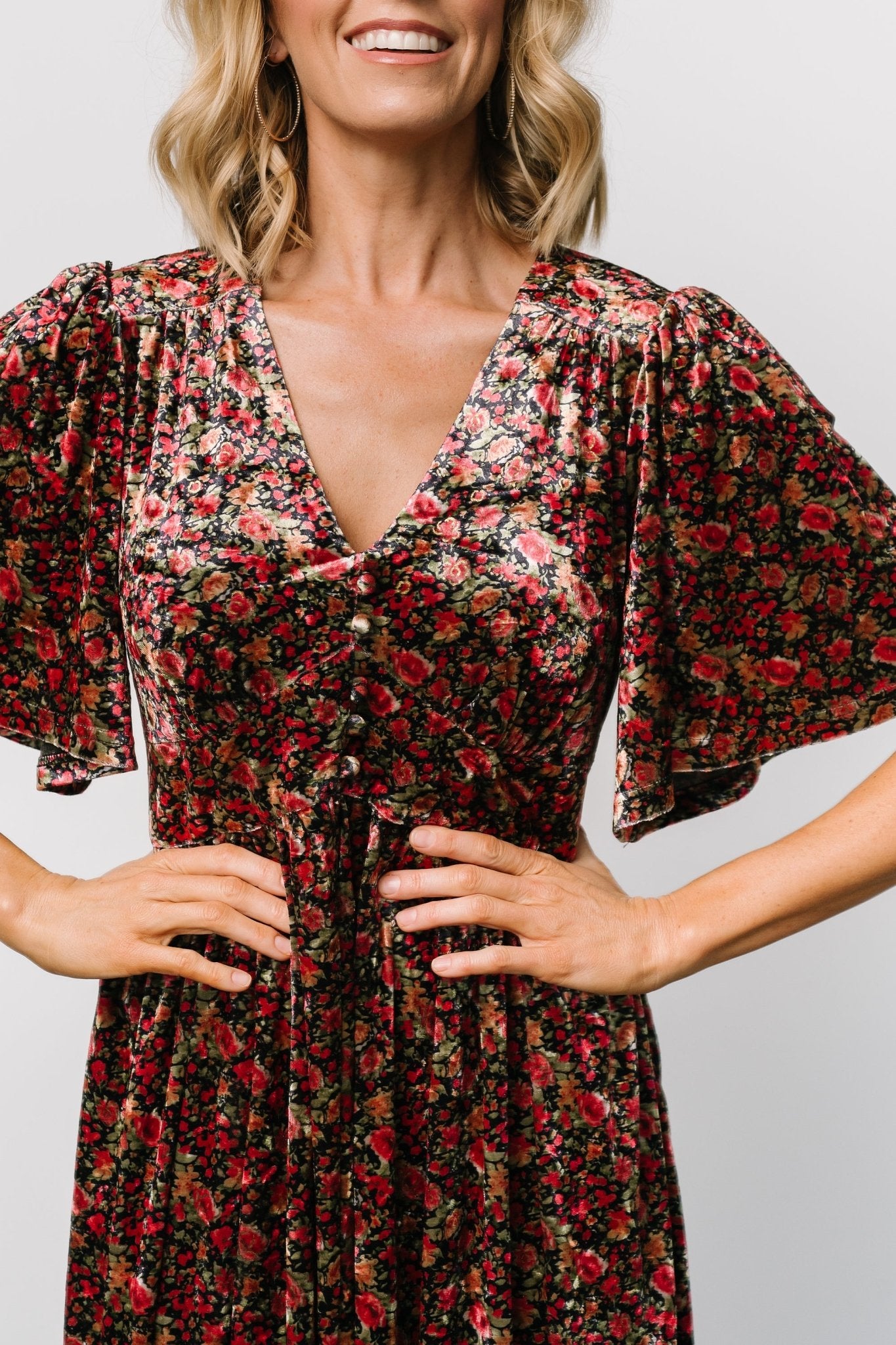 Three-quarter model view of the Irina Velvet Maxi Dress in black multi floral highlighting the empire waist, smocked back, and flutter sleeves.