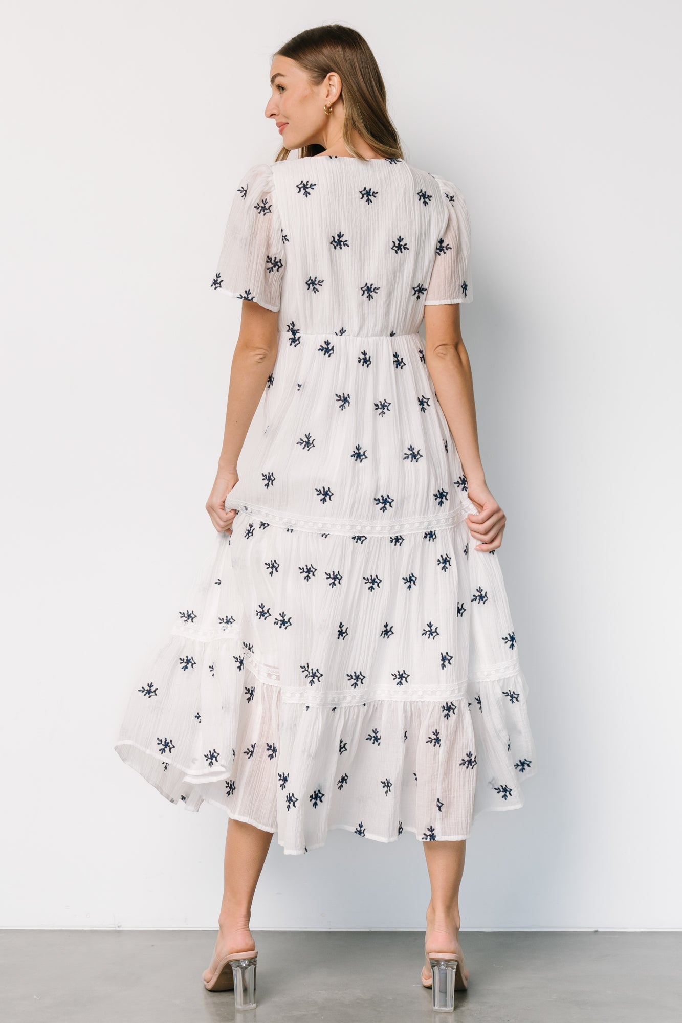 Styled outfit shot of off-white Jesenia dress with navy embroidery, illustrating midi length and flow when walking.