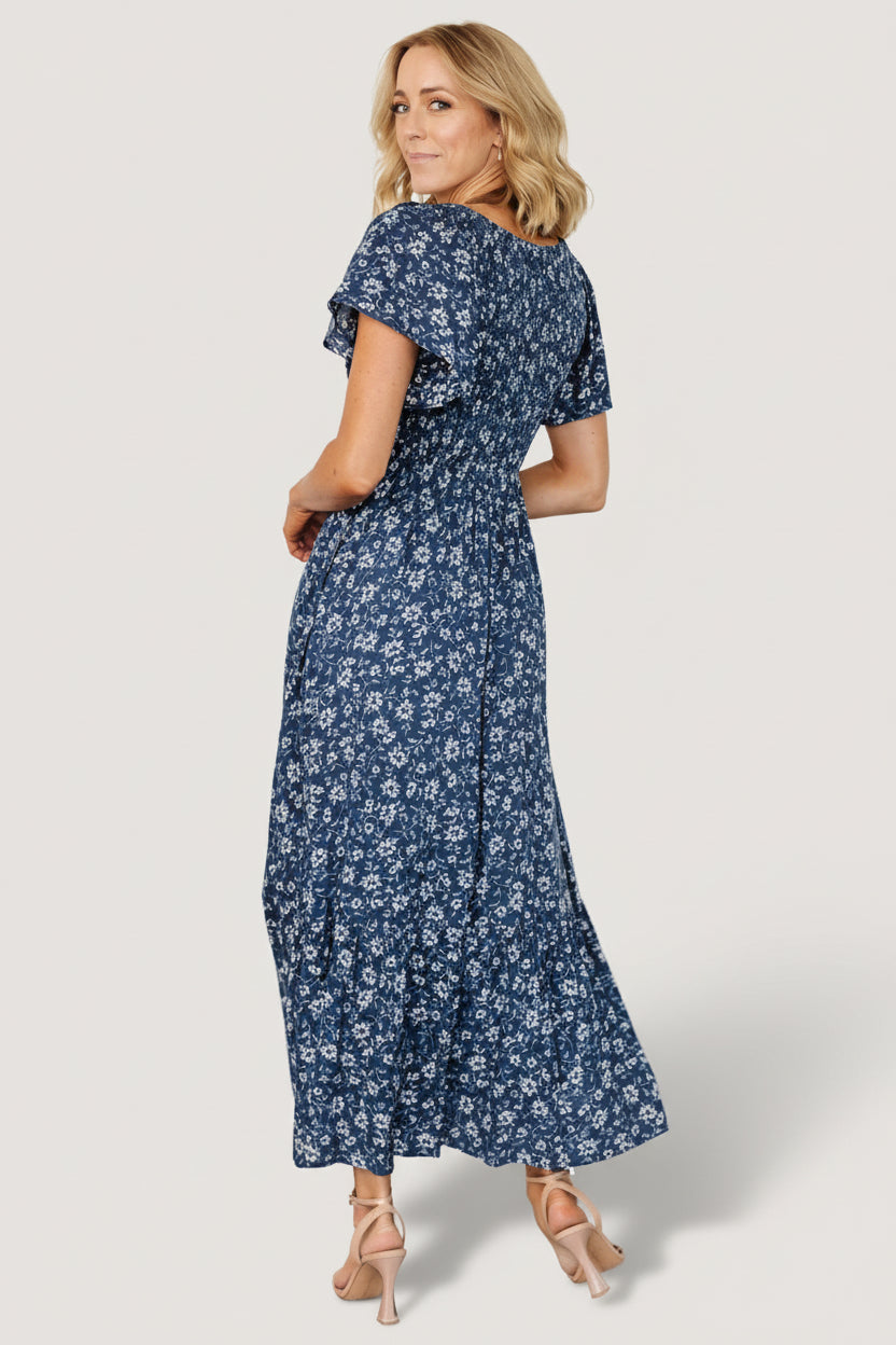 Model wearing Joanie Smocked Midi Dress in blue floral, styled with sandals to show length and natural drape.