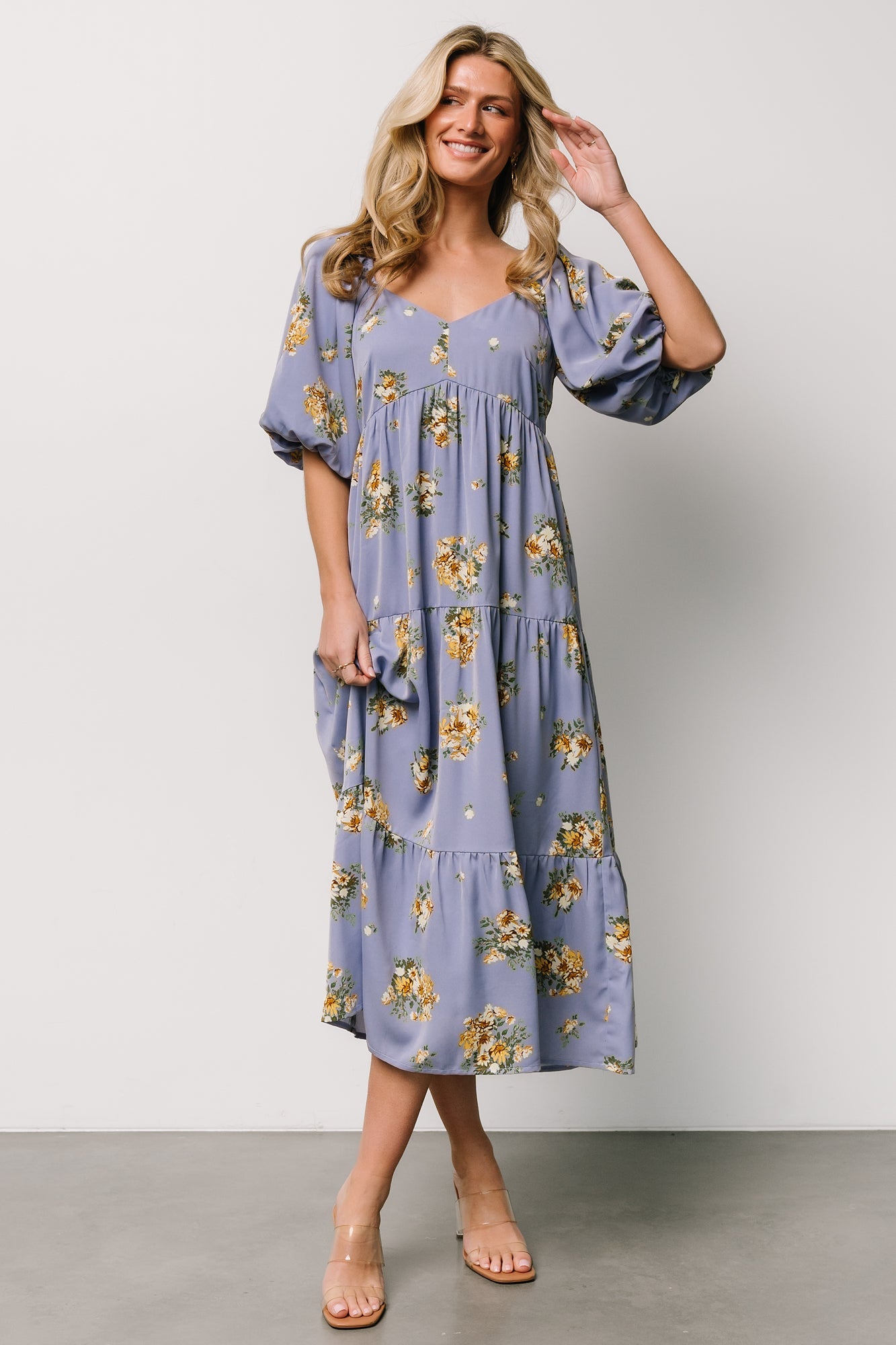 Model wearing Judith dress in blue with gold floral pattern showing oversized raglan balloon sleeves and elastic cuffs, side pockets visible.