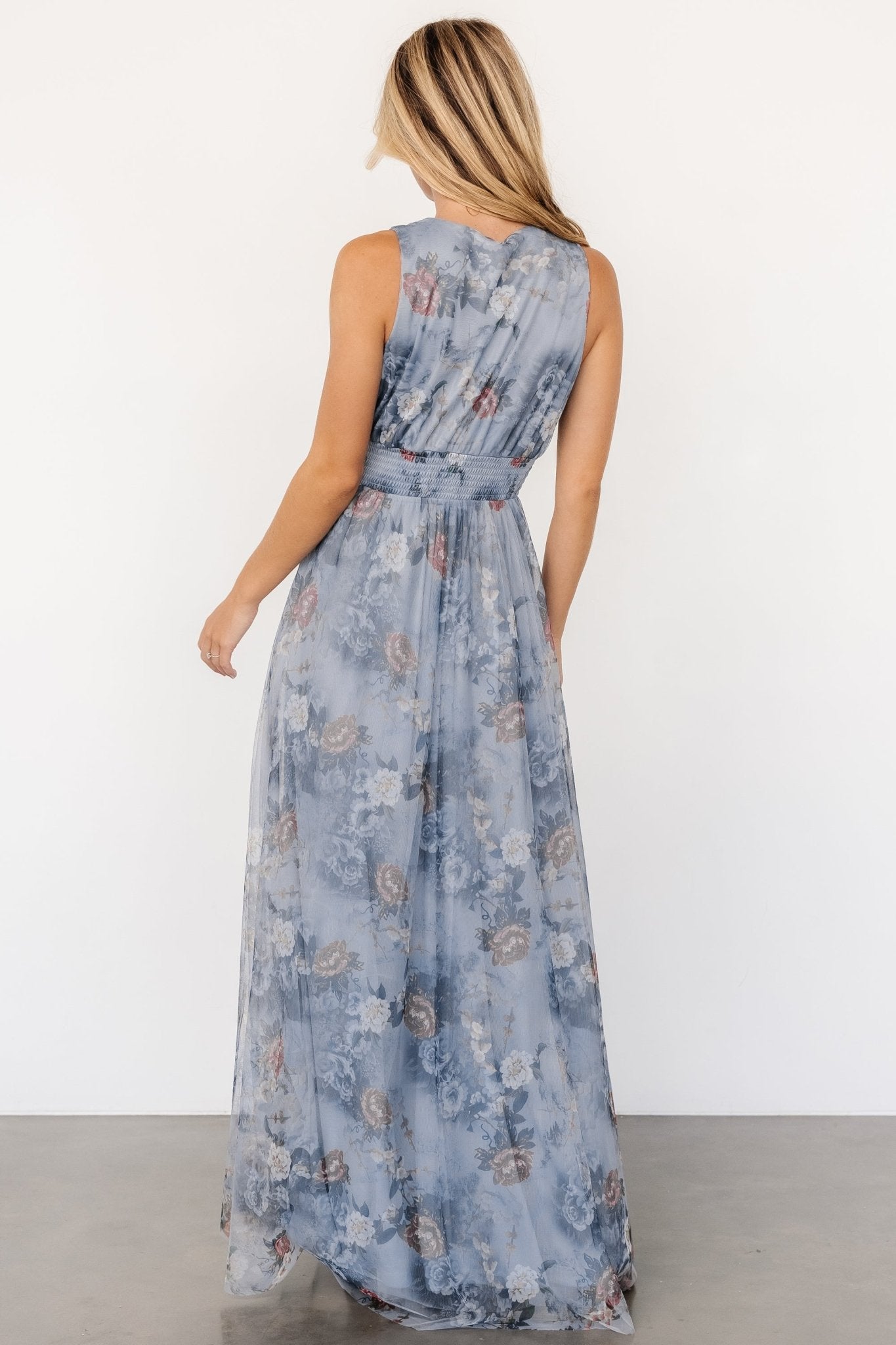 Back view of dusty blue floral tulle maxi dress on model, showing full lining, flowing skirt, and tank-style sleeve detail.