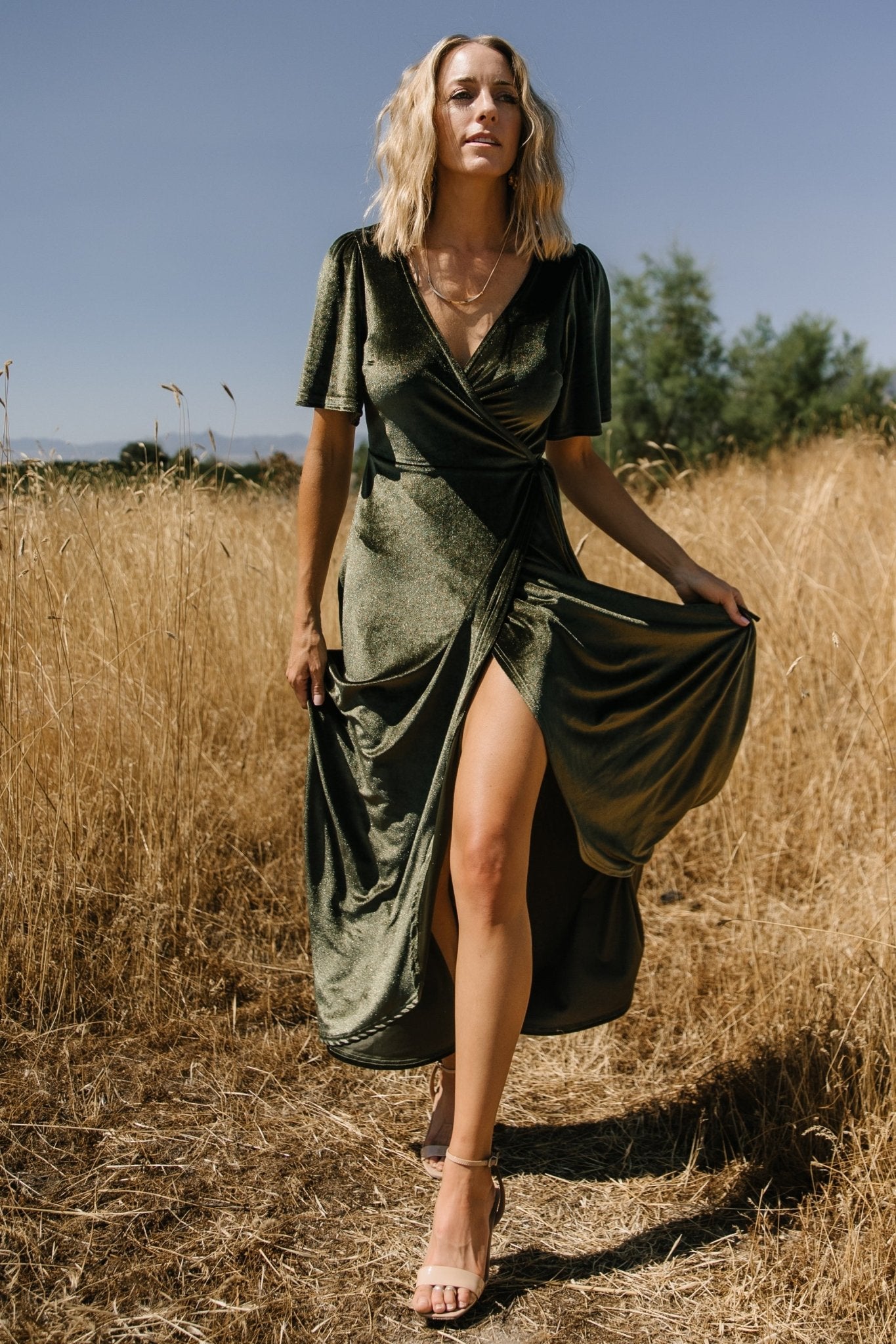 Model walking in the dark olive velvet wrap dress, highlighting skirt movement, lining coverage, and flattering wrap fit.