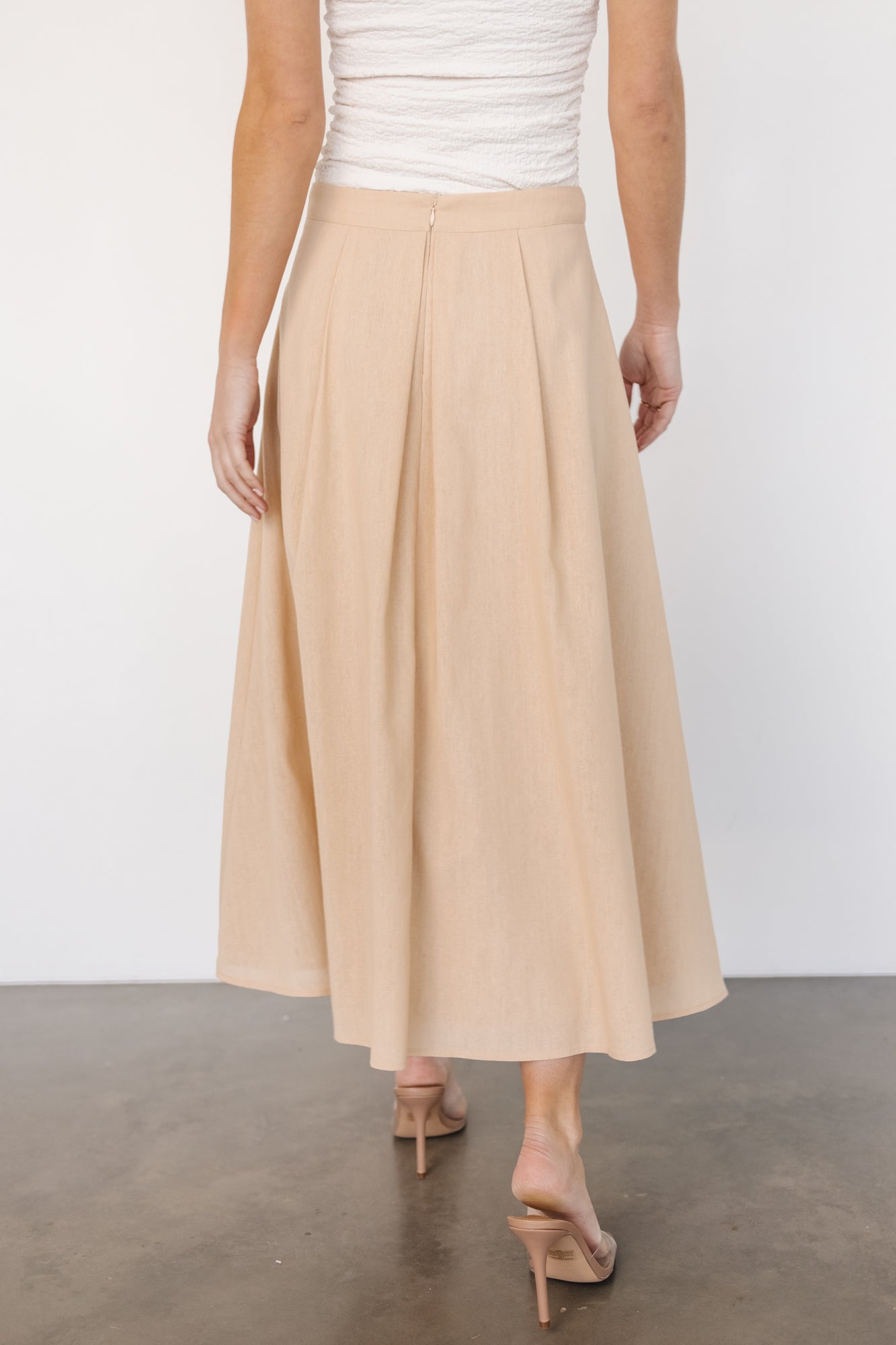 Styled flat-lay of pleated midi skirt in natural tone showing full lining, pleat density, and hem finish for styling reference.