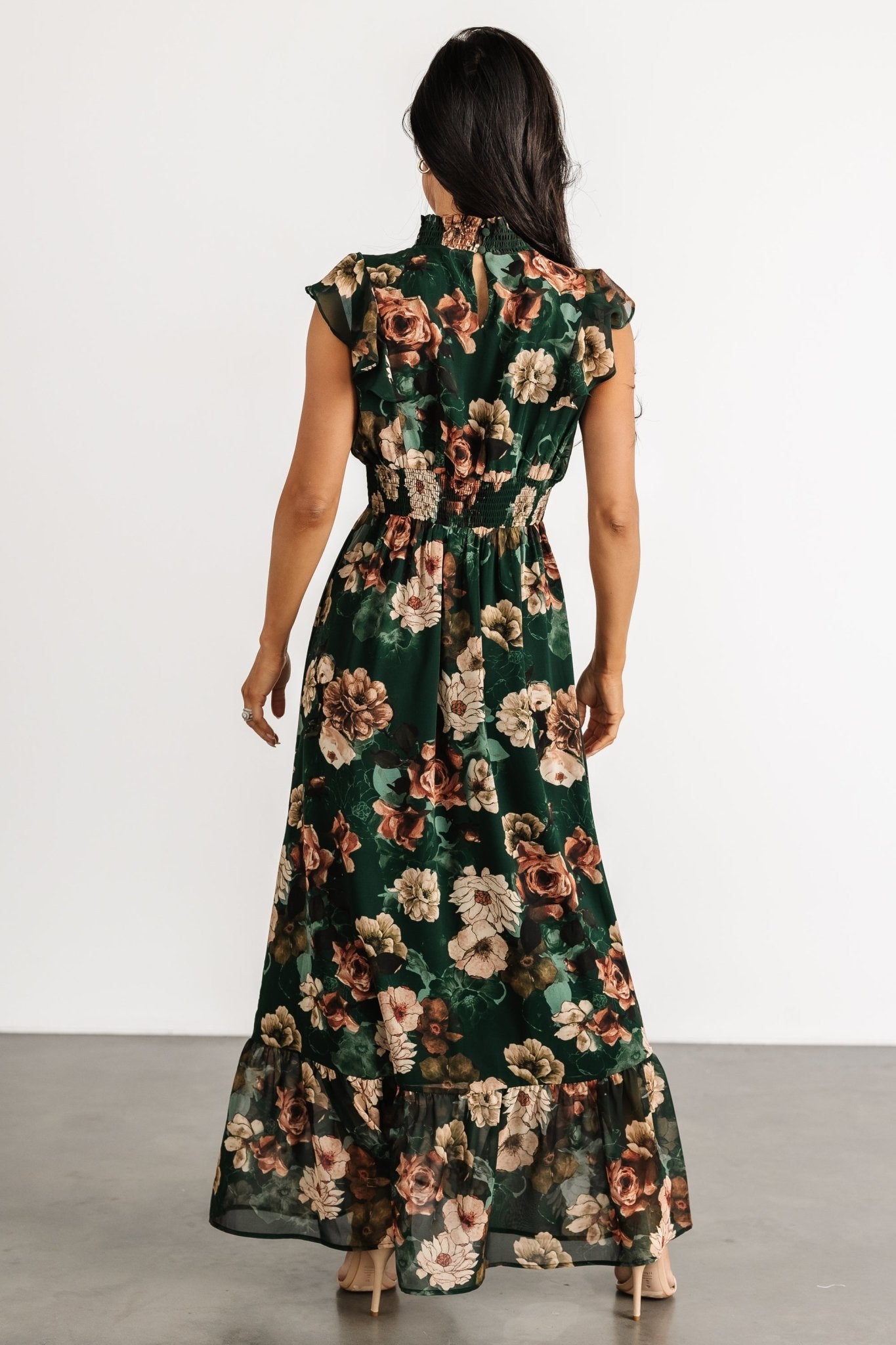 Back view of dark green floral maxi dress highlighting button closures at the neck, smocked waist shaping, and flowing skirt.