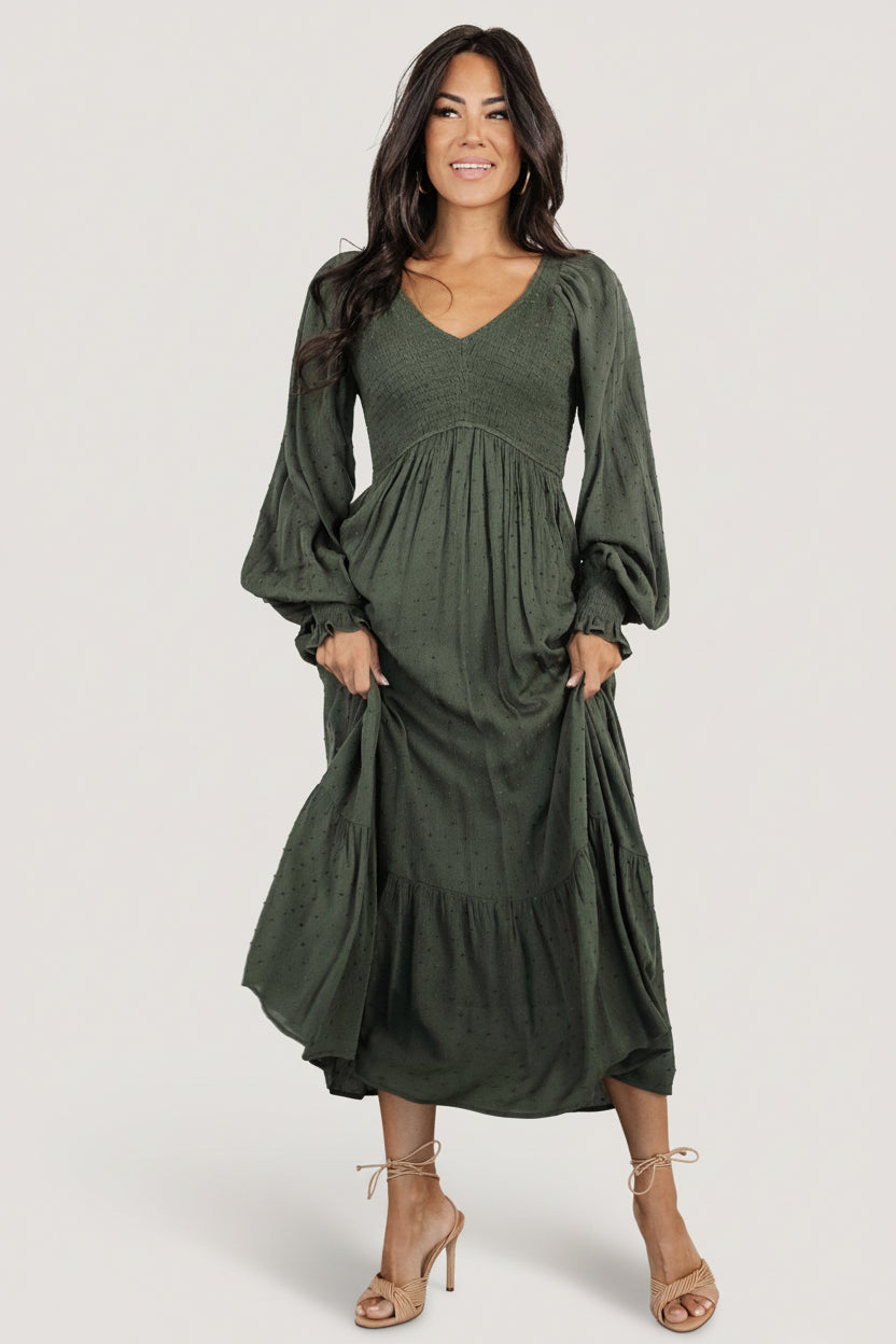 Detail image showing V‑neckline and elastic waist of the deep olive smocked dotted midi dress on a model.